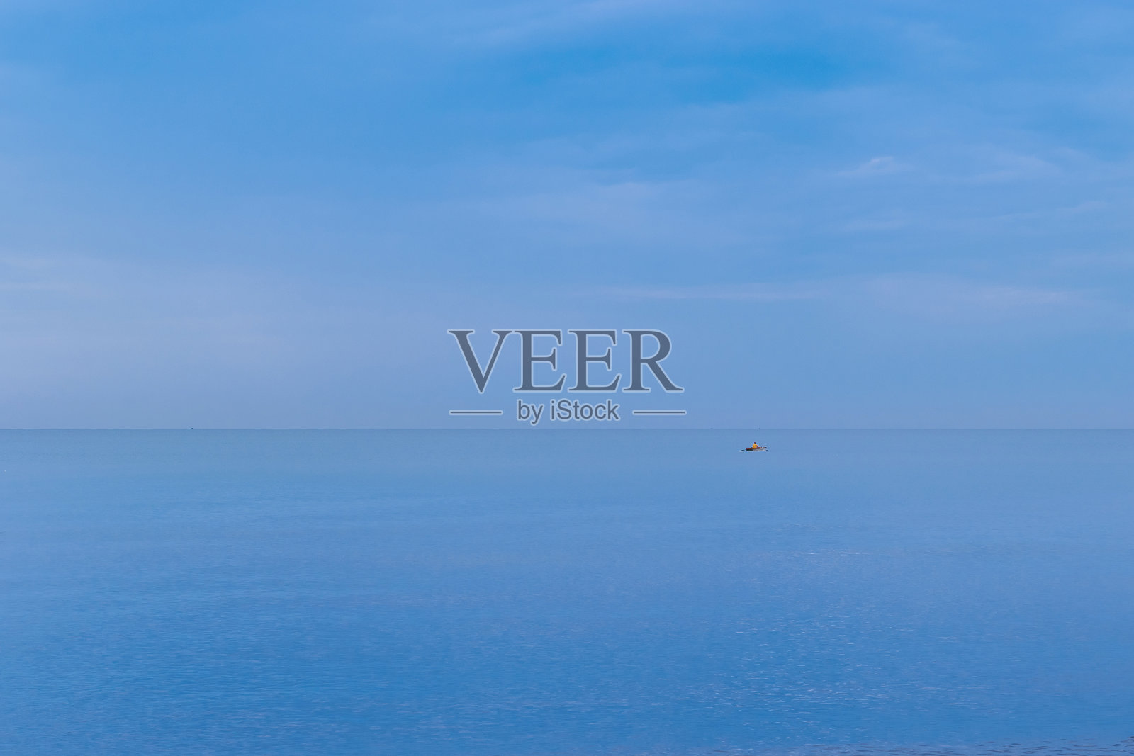 风平浪静的大海,忧郁的日子里,一个穿着黄色夹克的孤独的渔夫在他的小船上照片摄影图片