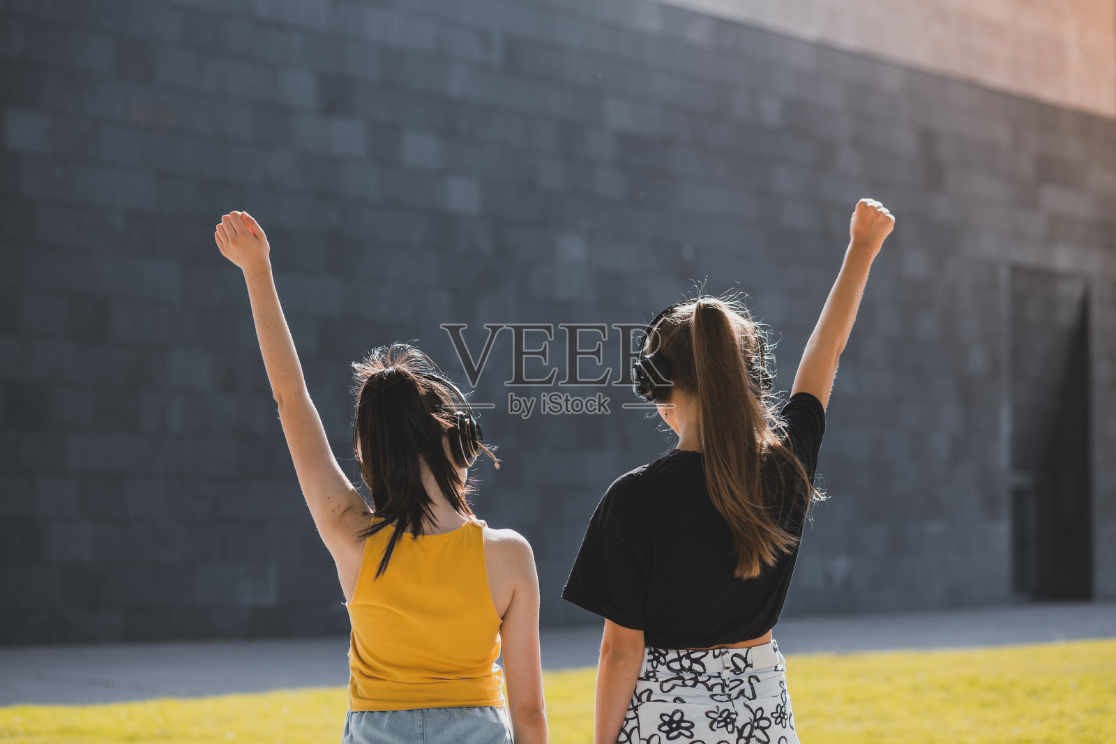 两个十几岁的女孩一边享受夏日,一边戴着耳机听着她们最喜欢的音乐。照片摄影图片