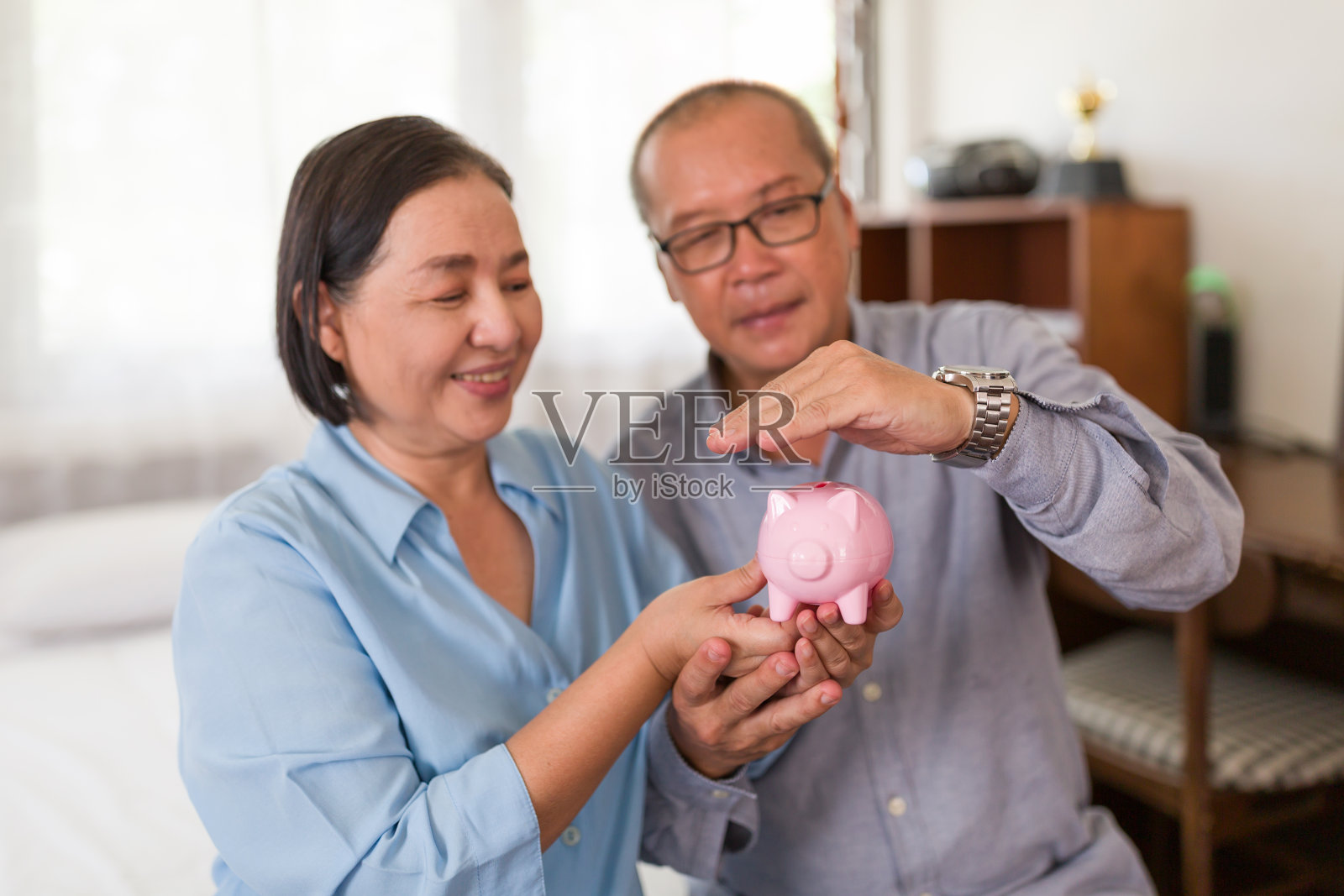 快乐的资深亚洲夫妇举起手盖在粉色小猪储蓄罐上面。退休、老龄化、存钱和理财观念照片摄影图片