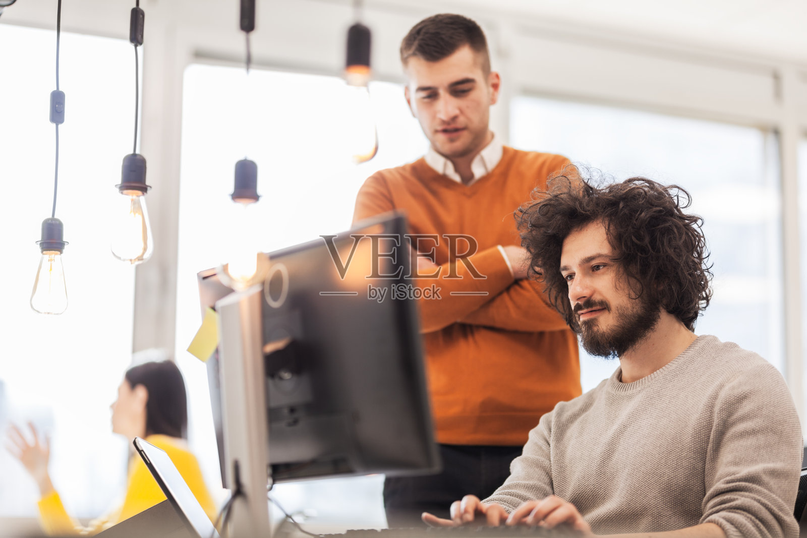 在现代的联合办公空间里,商务人士在电脑前交谈。照片摄影图片