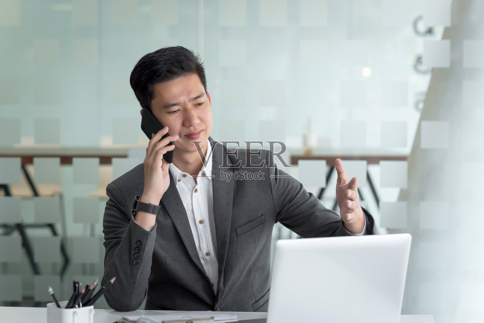 年轻的亚洲商人在办公室里和一个带着笔记本电脑的客户打电话。照片摄影图片