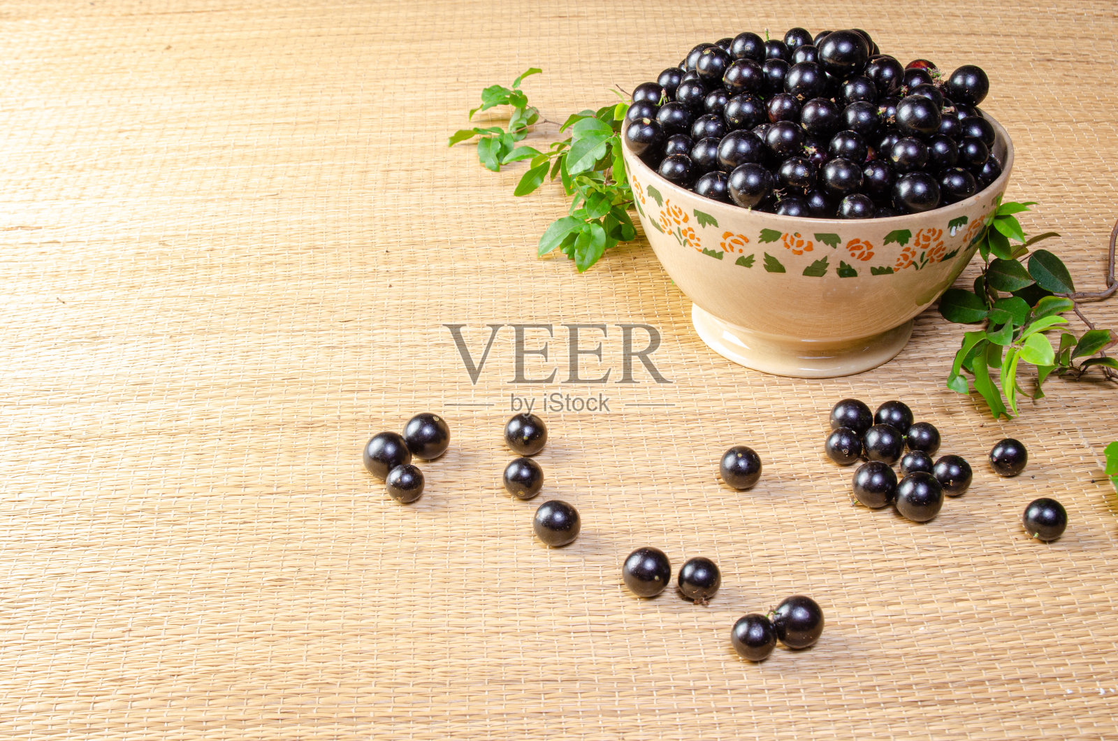 Jabuticaba,新鲜收获的Jabuticaba,还没有洗过,树枝和叶子放在一个漂亮的陶瓷碗上的草席,选择性的焦点。照片摄影图片