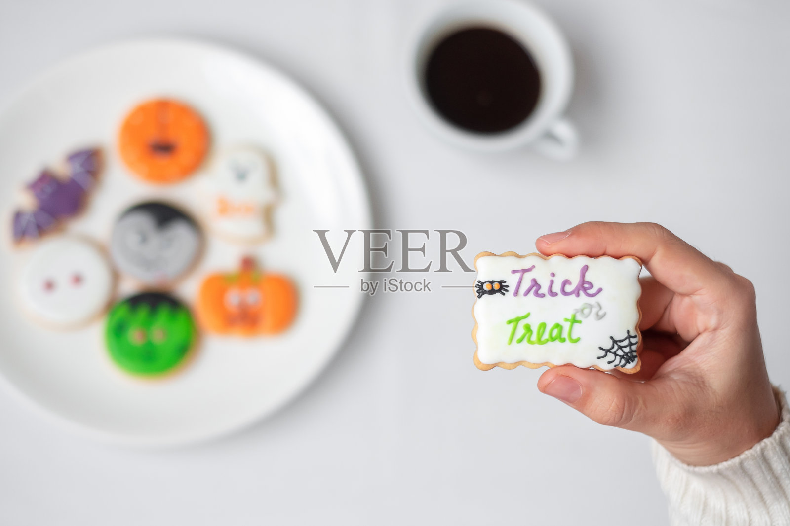 喝咖啡时,女人手里拿着有趣的万圣节饼干。万圣节快乐,恶作剧或威胁,你好十月,秋天秋天,传统,派对和节日概念照片摄影图片