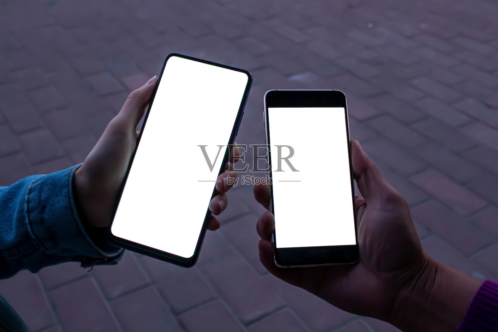 两名妇女使用手机与空白的白色桌面屏幕与街道背景。照片摄影图片