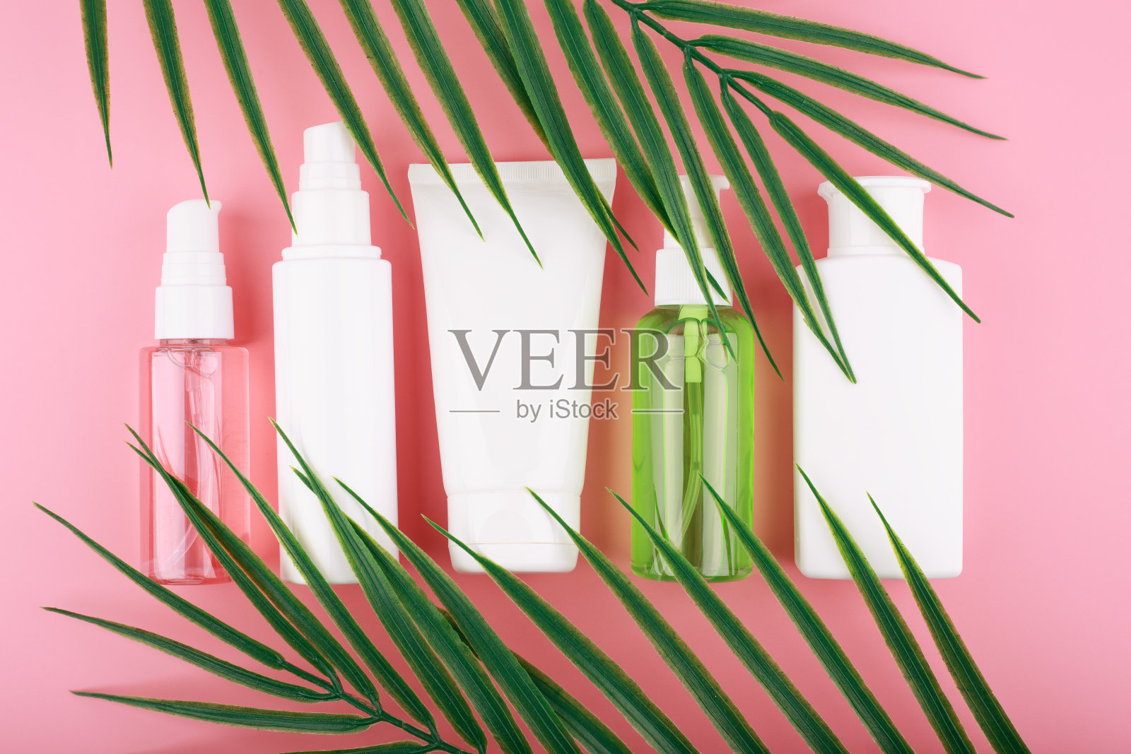 在粉色的背景上,用棕榈叶装饰化妆品照片摄影图片