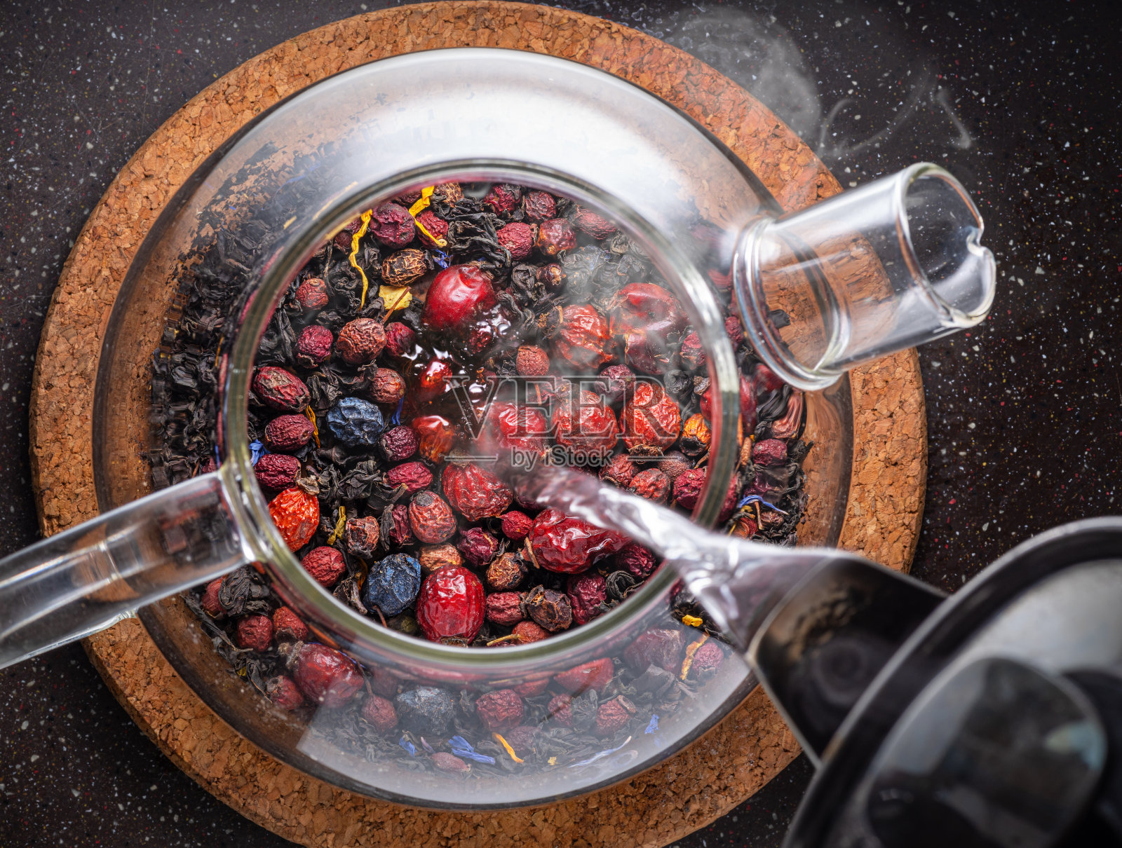 把热水倒进玻璃茶壶里,把干浆果和花合起来。前视图。照片摄影图片