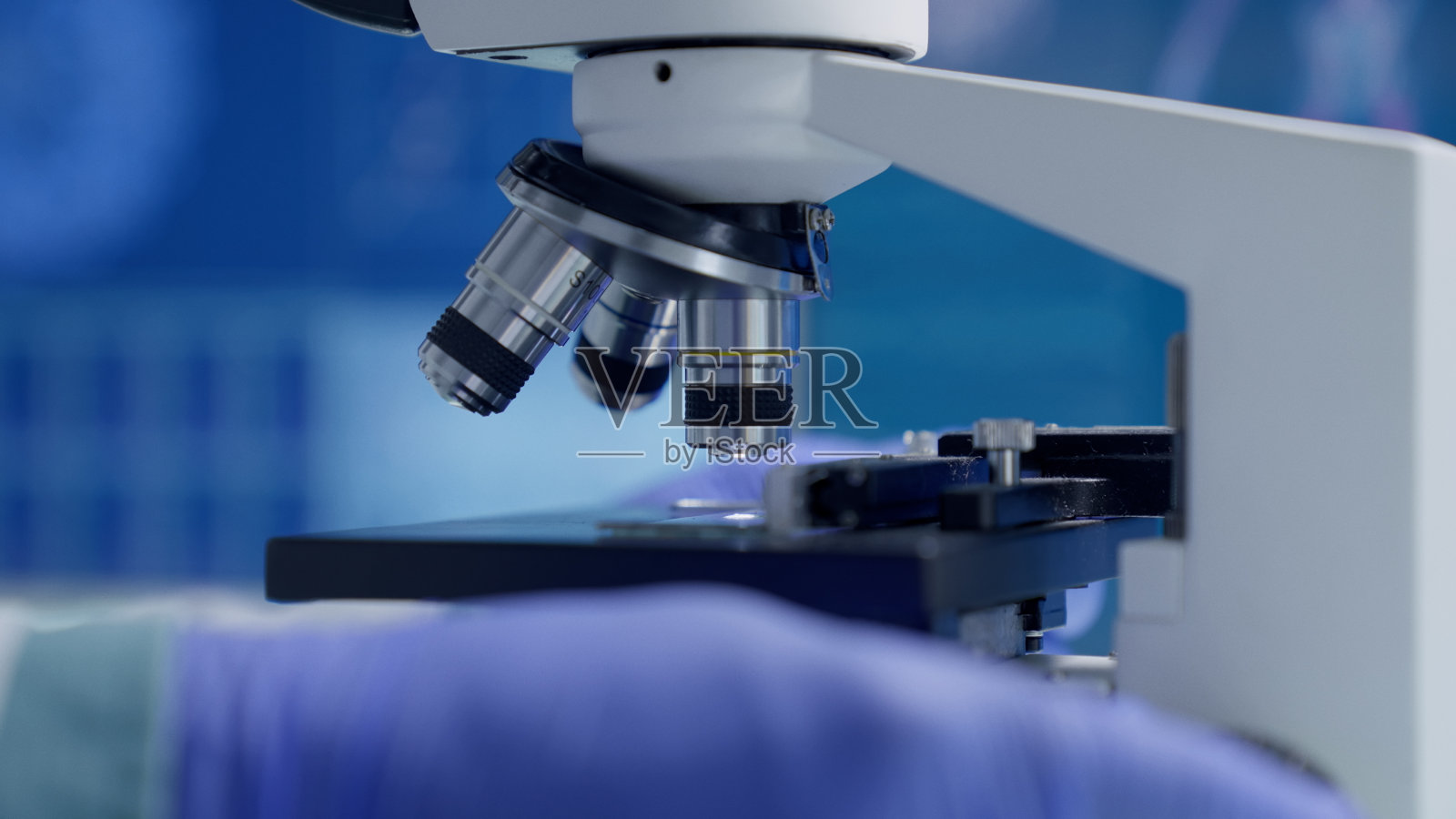 科学家在研究室校准显微镜。靠近手部。背景中有DNA和骨骼模型的屏幕照片摄影图片