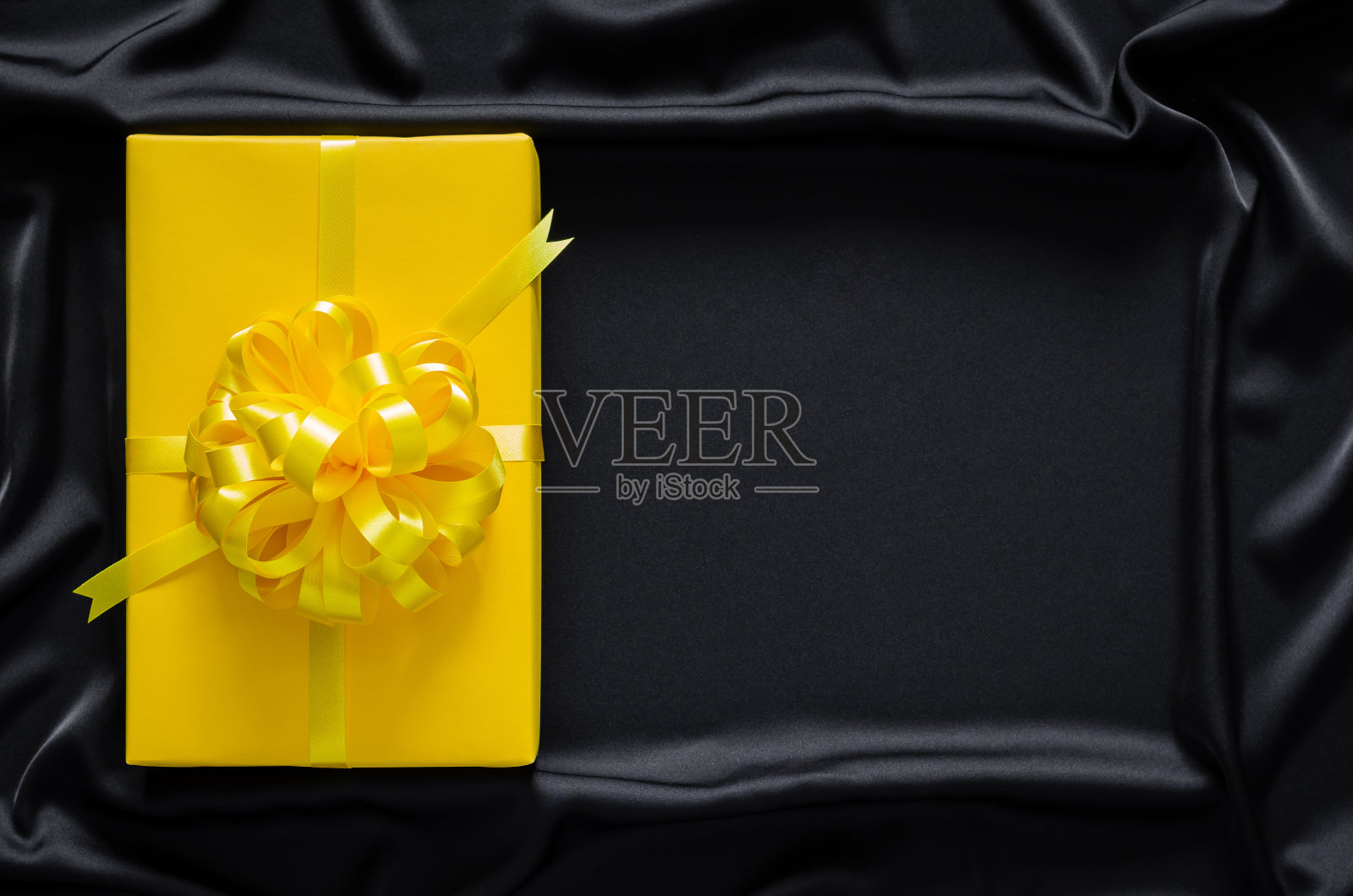 一个带丝带的黄色礼品盒放在黑色光滑的波浪布上照片摄影图片