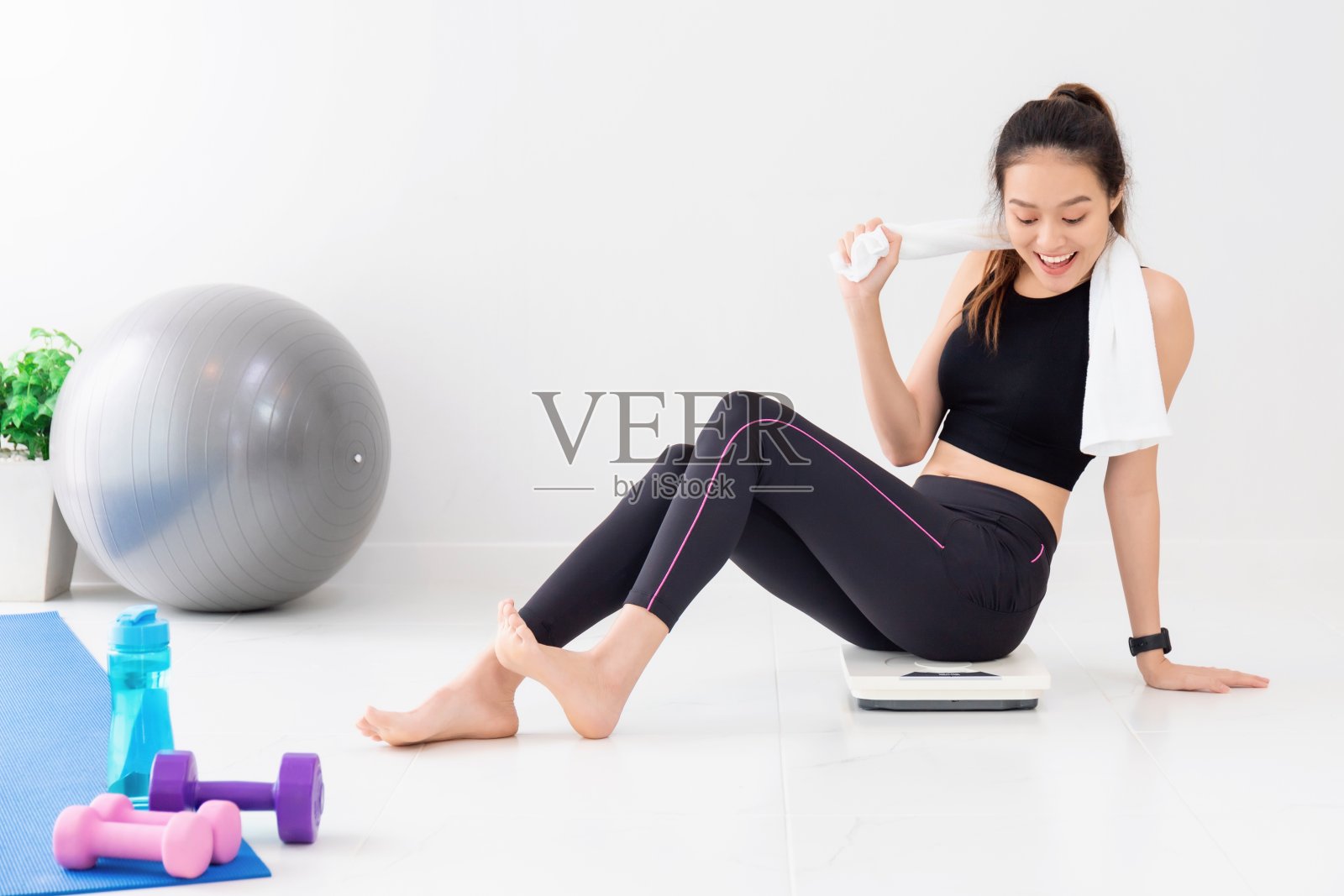 亚洲快乐美丽的女人休息后的锻炼和坐在体重秤在家里的健身房背景。运动减肥,增加柔韧性,紧致体形。照片摄影图片