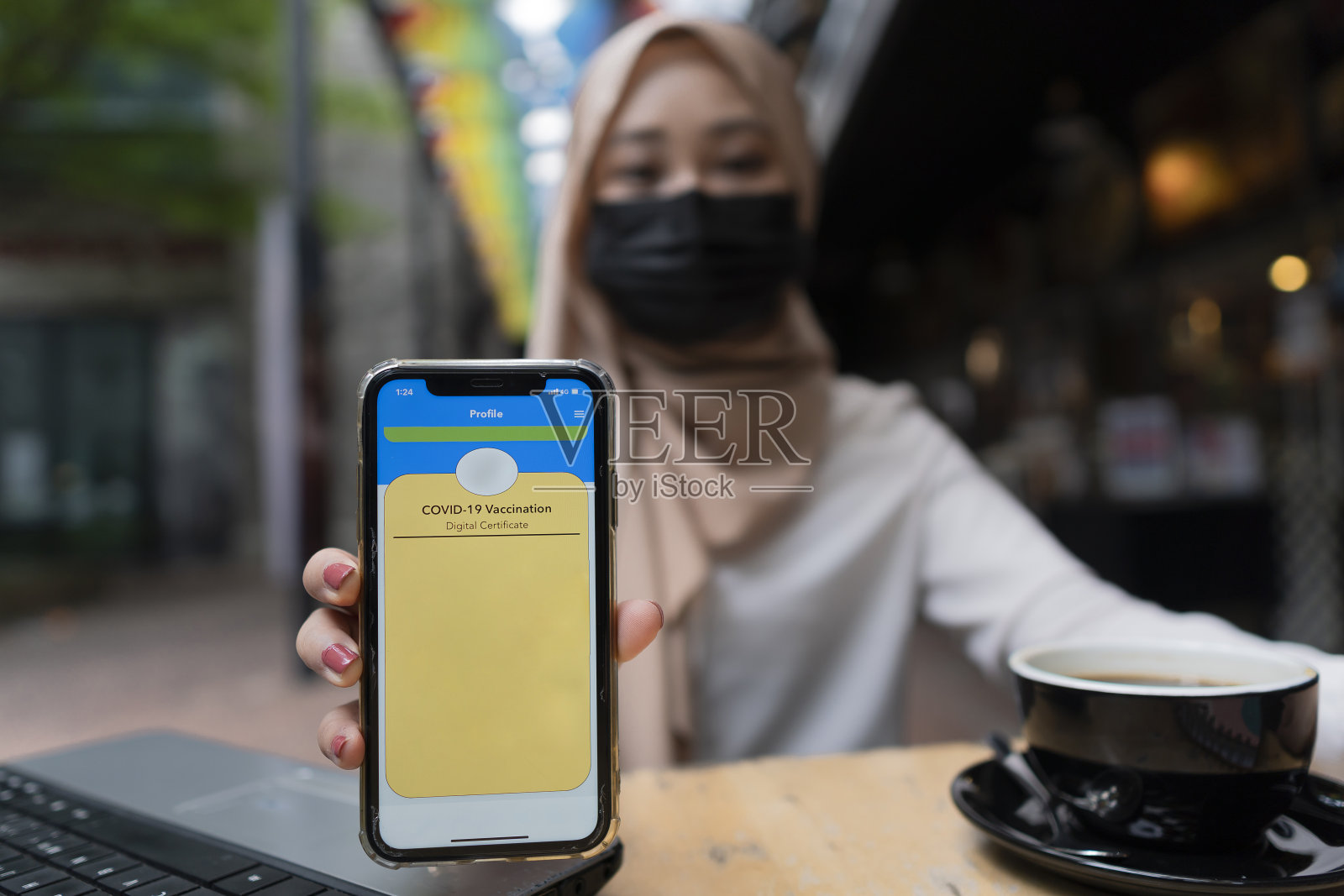 已接种疫苗的马来人女士在咖啡店用餐,用智能手机出示疫苗证书照片摄影图片
