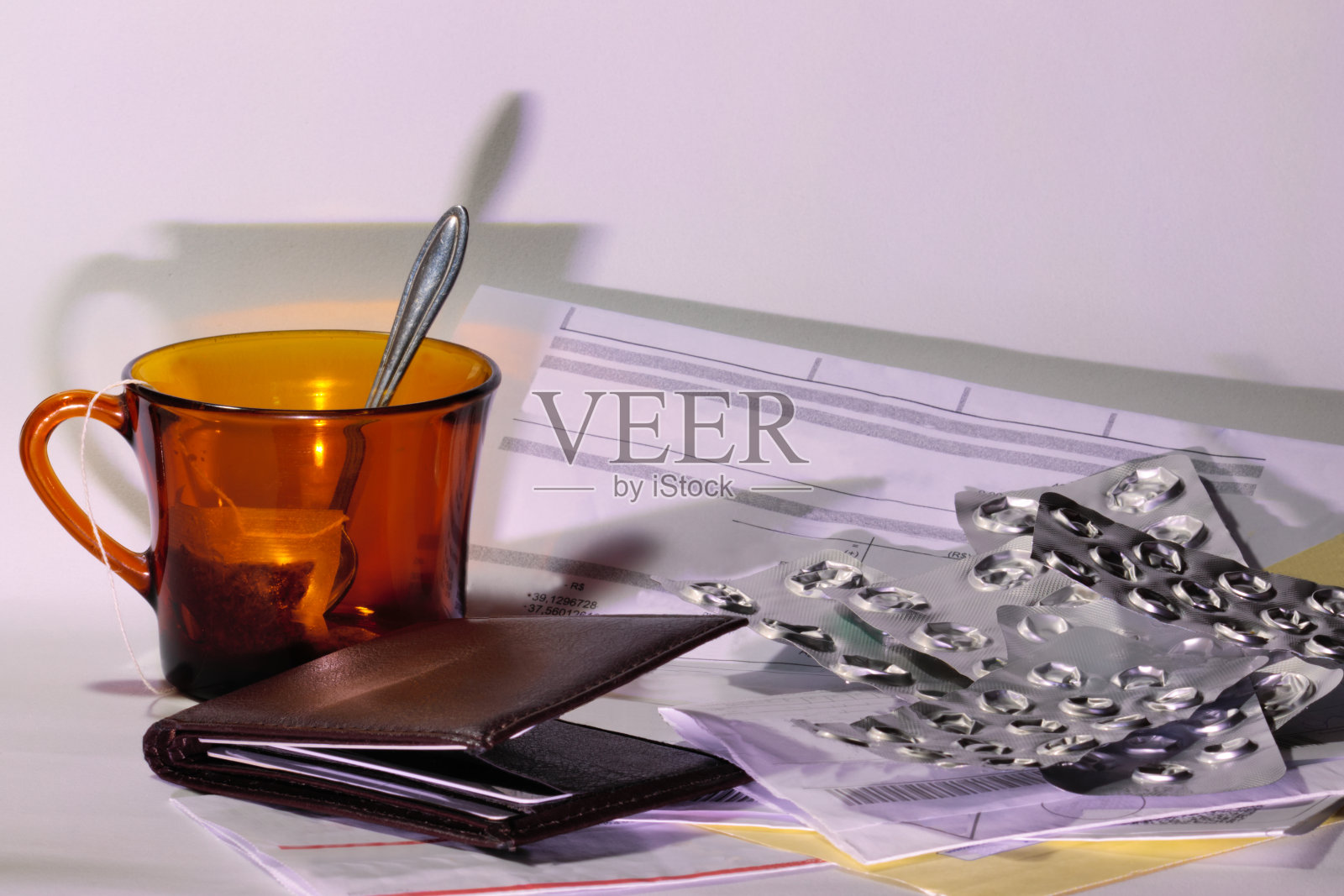 有茶包和勺子的杯子,旁边是钱包、要付的账单和空医药卡,白色背景下。照片摄影图片