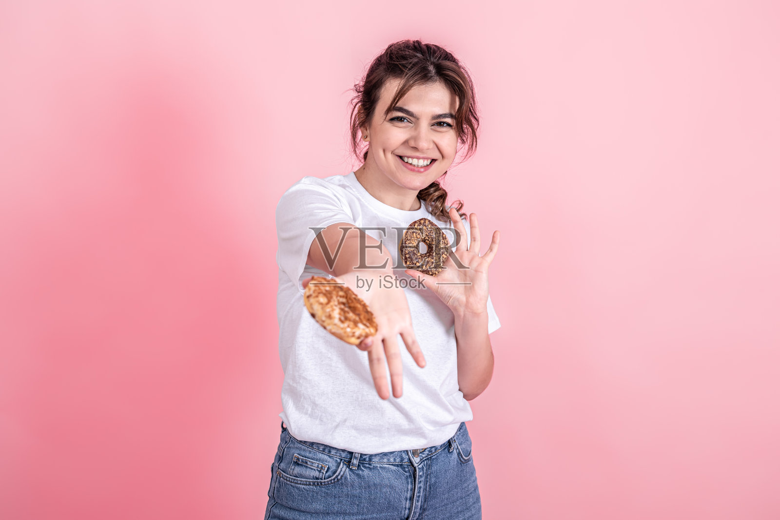 一个漂亮的,年轻的女人的肖像展示甜甜圈孤立在粉红色的背景。照片摄影图片