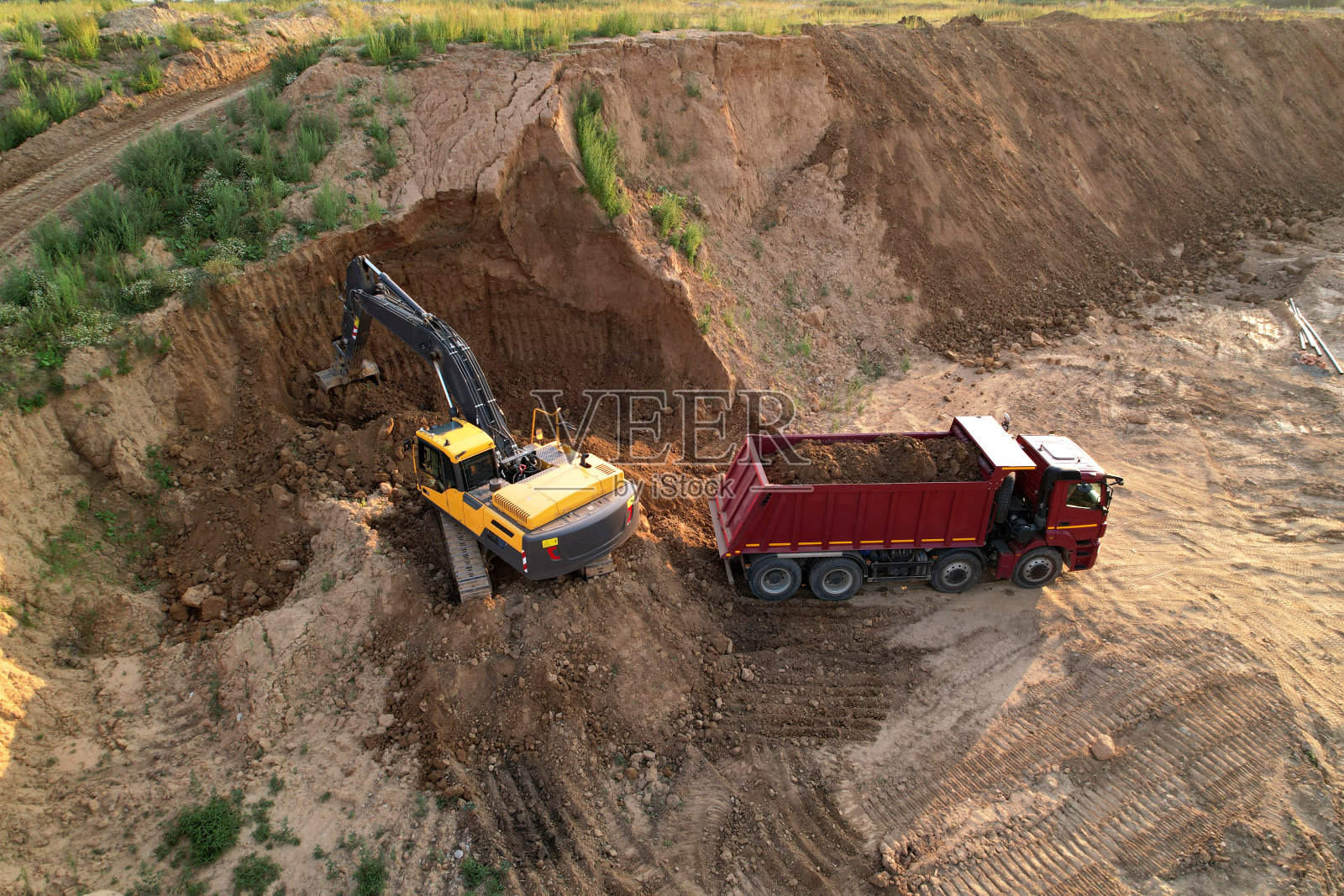 挖掘机将沙子装入自卸卡车,装载机为地基坑挖掘地面,在建筑工地进行土方作业照片摄影图片