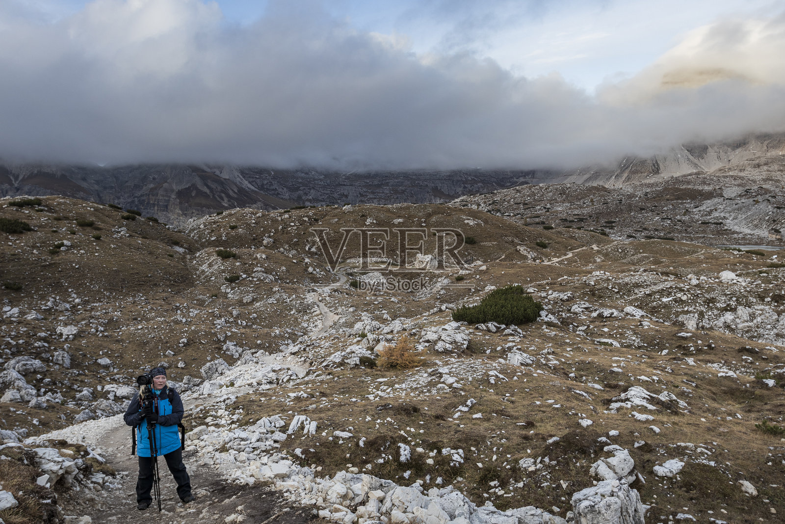 一名身穿蓝色夹克的女子、一名游客、一名摄影师,在意大利多洛米特山脉的Tre Cime Lavaredo周围徒步旅行,背景是山脉和蓝天和白云照片摄影图片