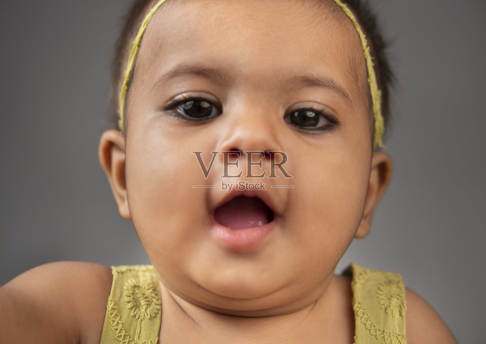 在灰色背景下,可爱的小女孩穿着漂亮的绿色连衣裙。照片摄影图片