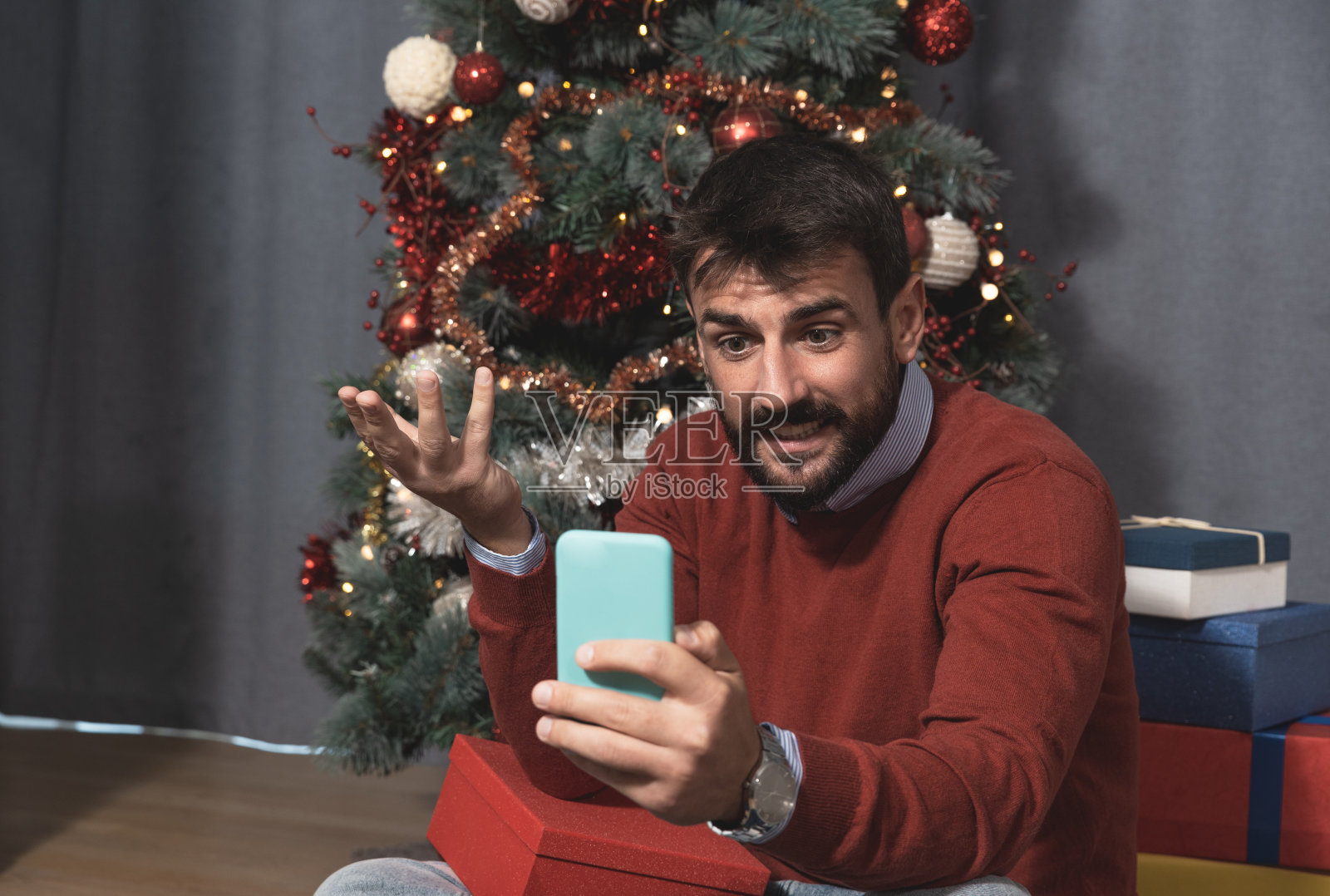 年轻的快乐和担心的男人打电话给他的女朋友在智能手机视频电话,问她在哪里,为什么她在圣诞晚会和新年前夕迟到了,他正在等待她的礼物照片摄影图片