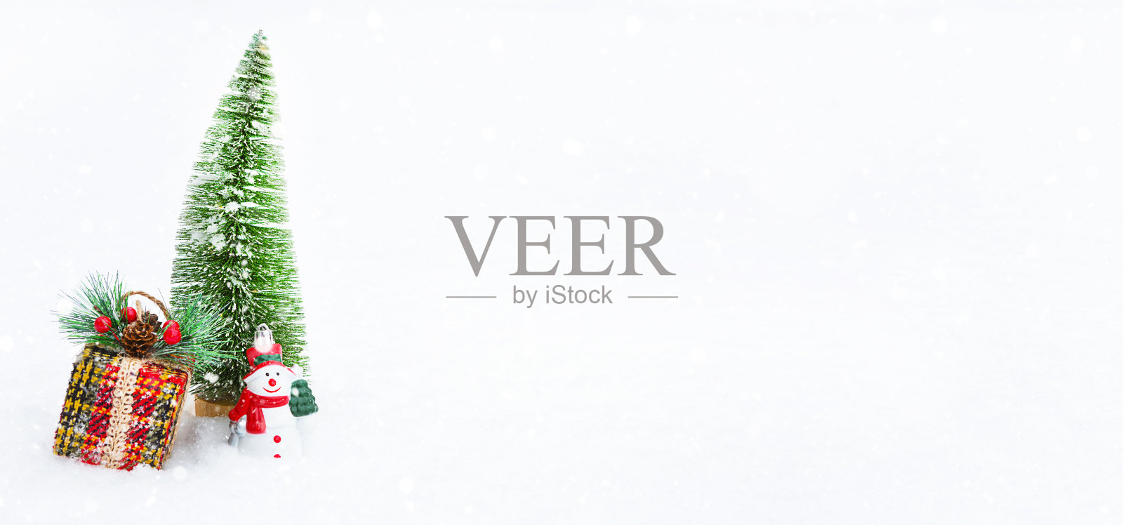 一棵圣诞树,一个礼品盒和一个玩具雪人在白色的天然雪中下雪。装饰新年和圣诞节,贺卡与copyspace照片摄影图片