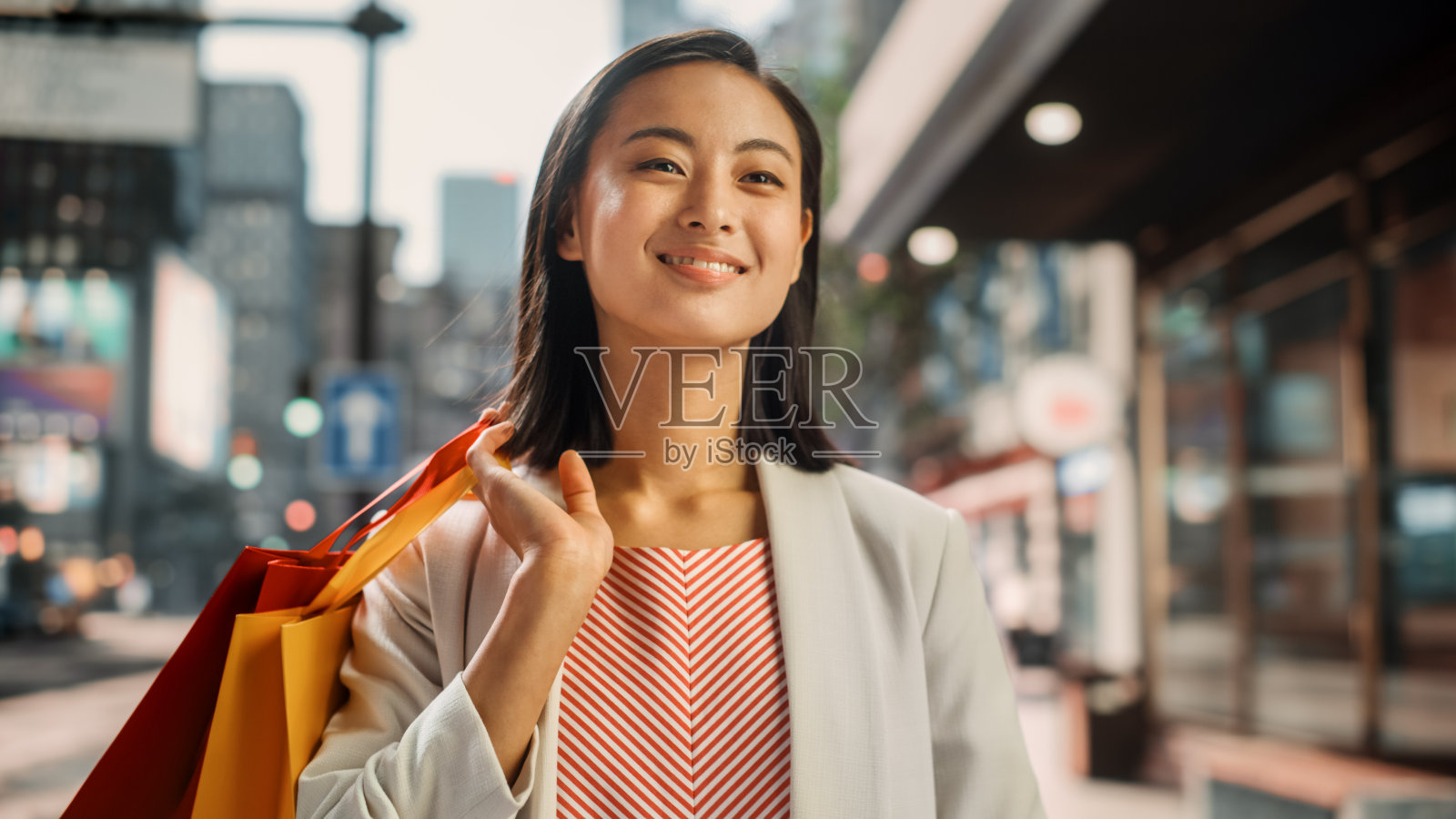 美丽的日本女性穿着时髦的休闲装在街上的肖像。成功的女性把购物袋放在她的肩膀在大城市环境中生活的城市生活方式。照片摄影图片