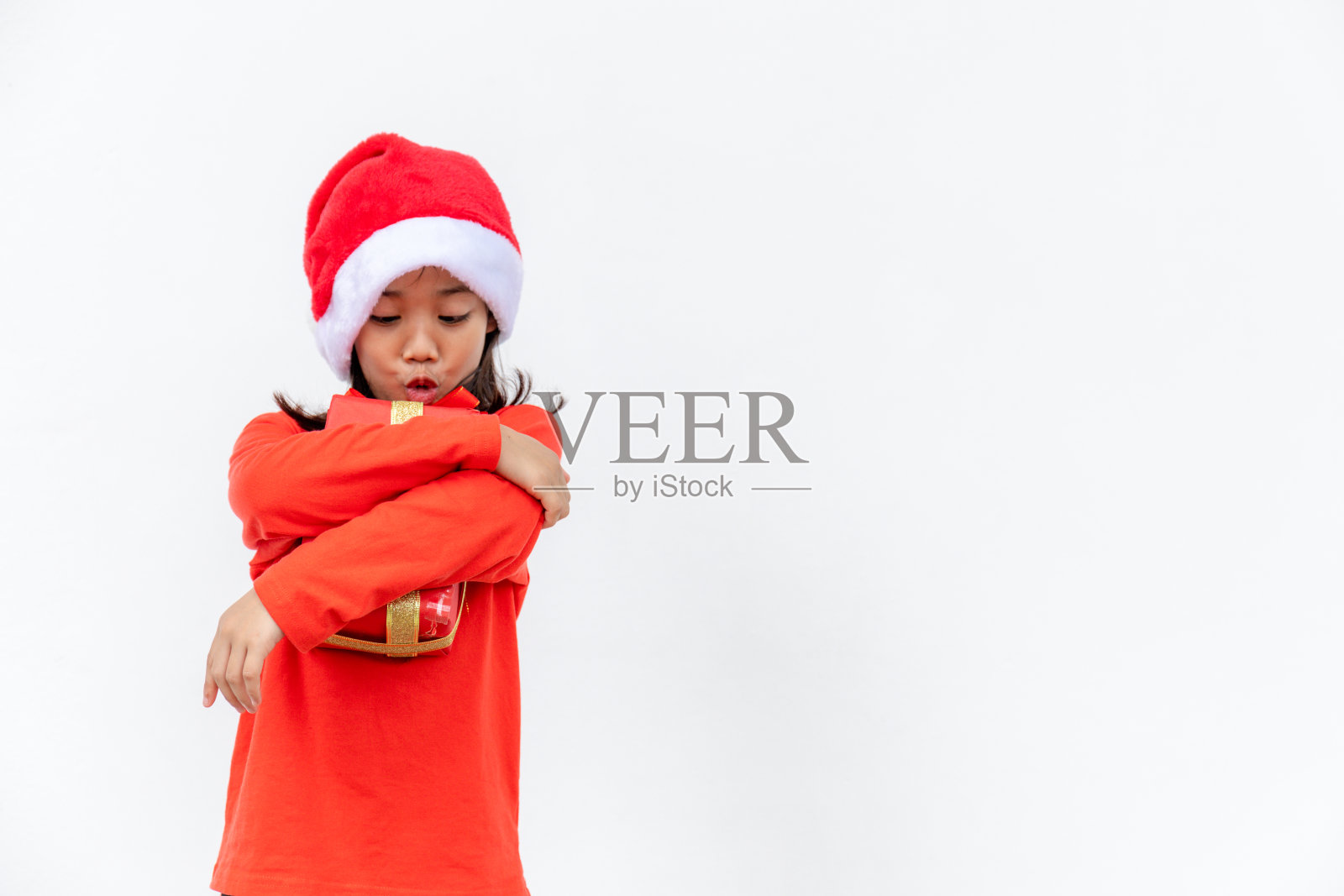 快乐的亚洲孩子戴着圣诞老人的红帽子,手里拿着圣诞礼物。圣诞节的时间。在白色背景上。照片摄影图片