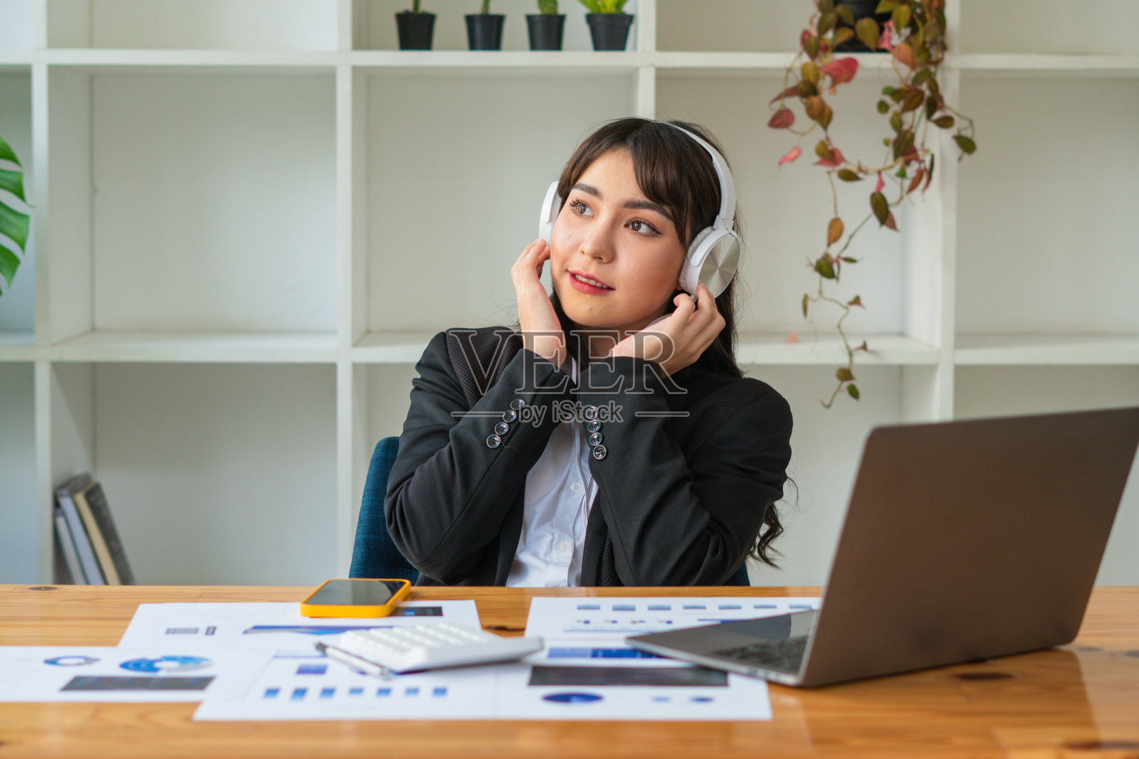 年轻的亚洲女性戴着耳机在办公室享受着音乐放松工作。照片摄影图片