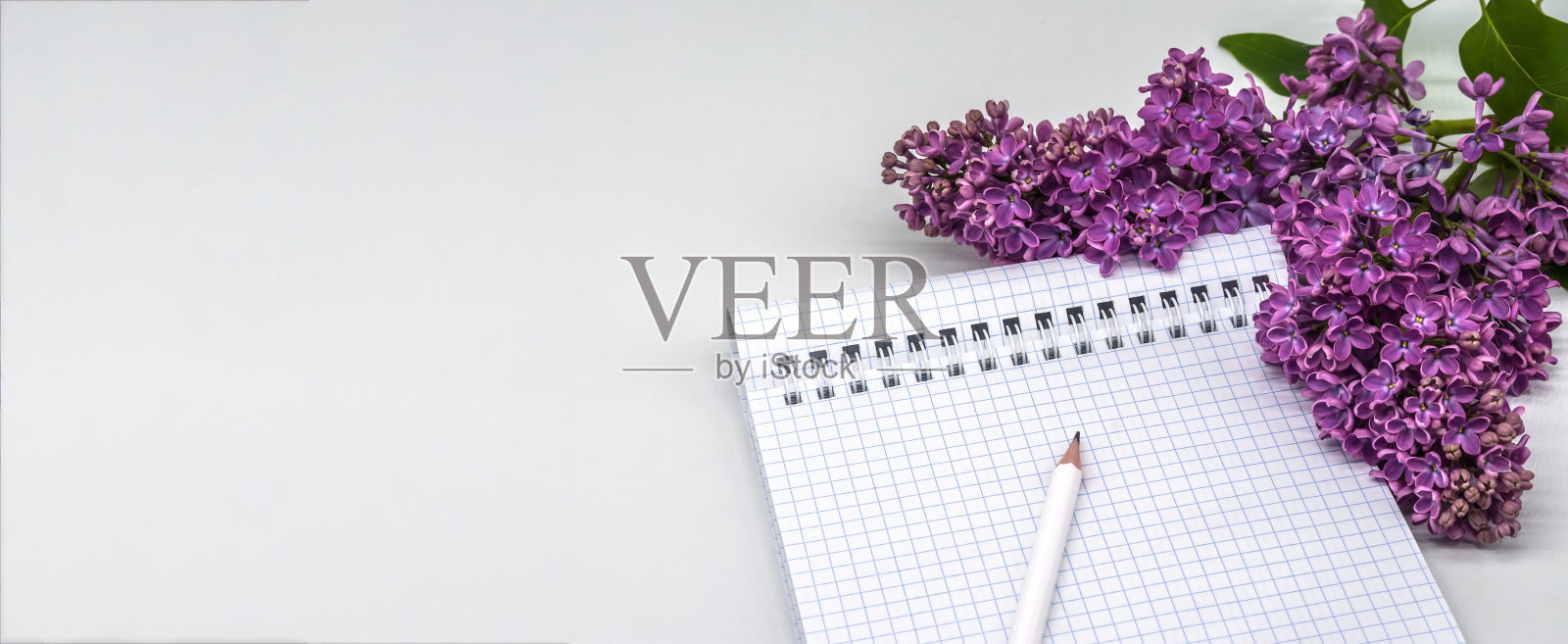 螺旋笔记本和笔。记事本上有笔和花。笔记本紫丁香在光的背景。照片摄影图片