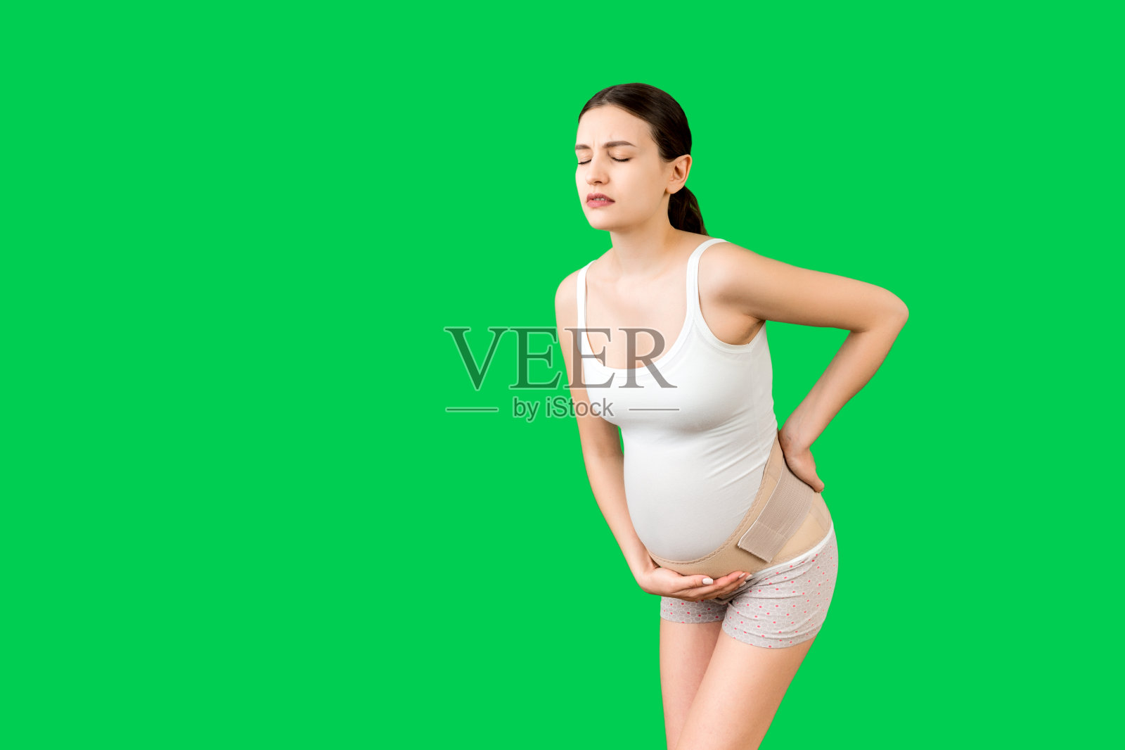 孕妇腰痛的支持绷带的肖像在绿色背景与复制空间。母亲背部疼痛。骨科腹部支撑带概念照片摄影图片