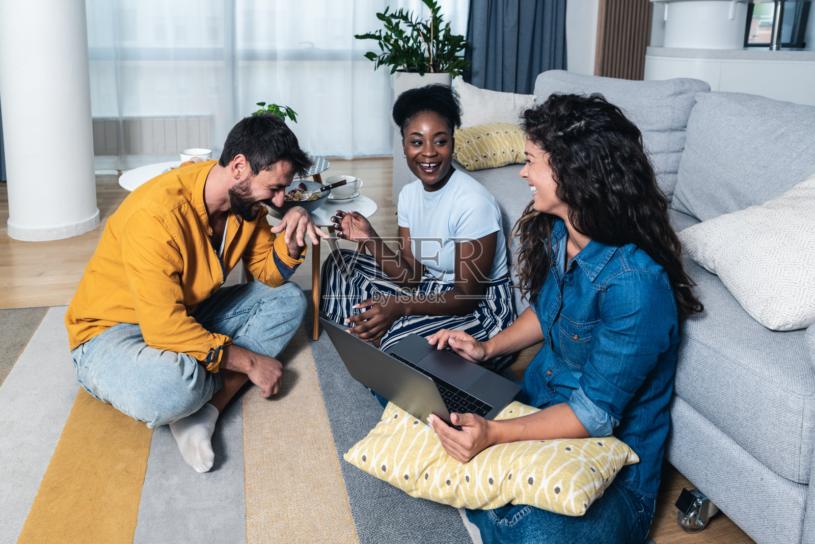 三位年轻的好朋友和商业伙伴坐在公寓里,庆祝他们在网站上的第一次网上销售。他们创办的公司是一家小型网上购物公司照片摄影图片