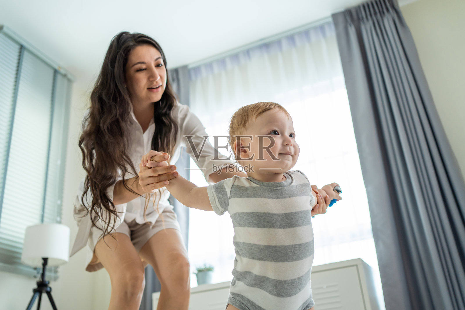 白种小可爱的小男孩在家里和父母一起学习走路。幸福的家庭母亲支持蹒跚学步的儿子在地板上迈出第一步,父亲在家里的客厅里发展技能照片摄影图片