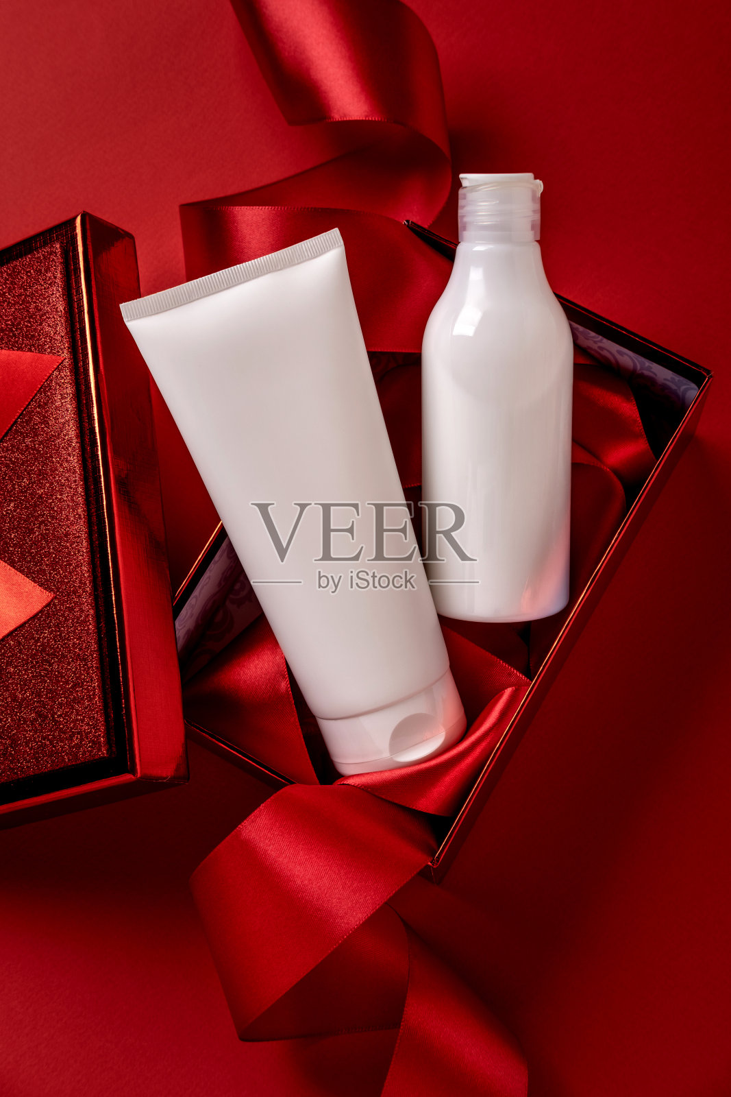 白色瓶子化妆品产品在红色礼品盒和红色背景。圣诞节销售美容产品概念。顶部视图与文本的位置。照片摄影图片