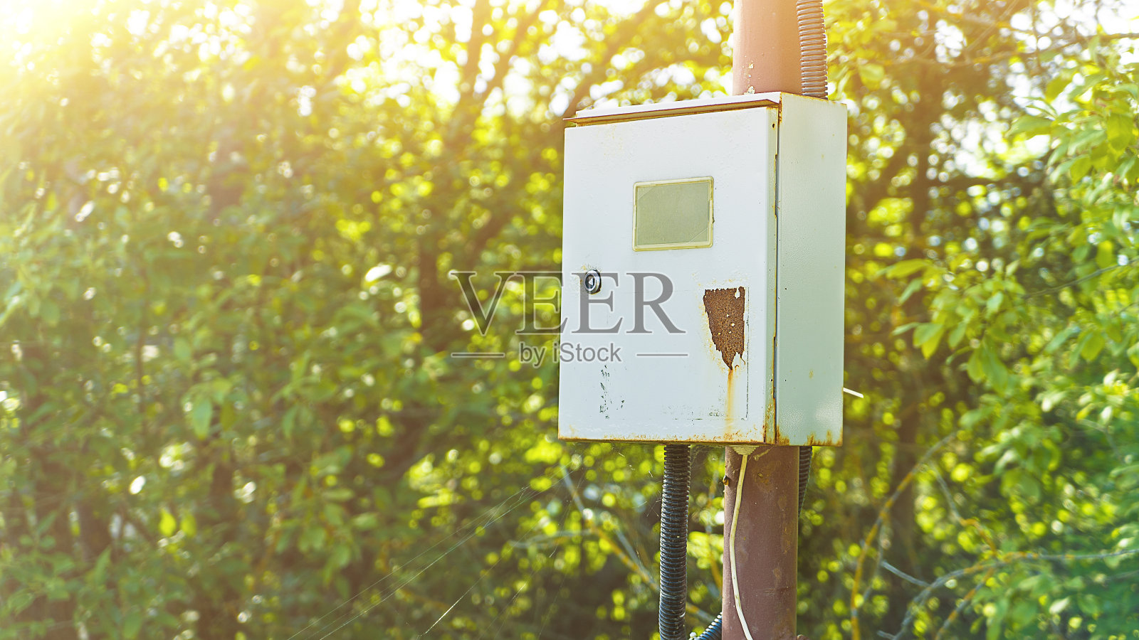 街上的电控箱。户外控制开关和电气开关。在一个晴朗的夏日,灰色的铰链把电源安装在一根铁柱子上照片摄影图片