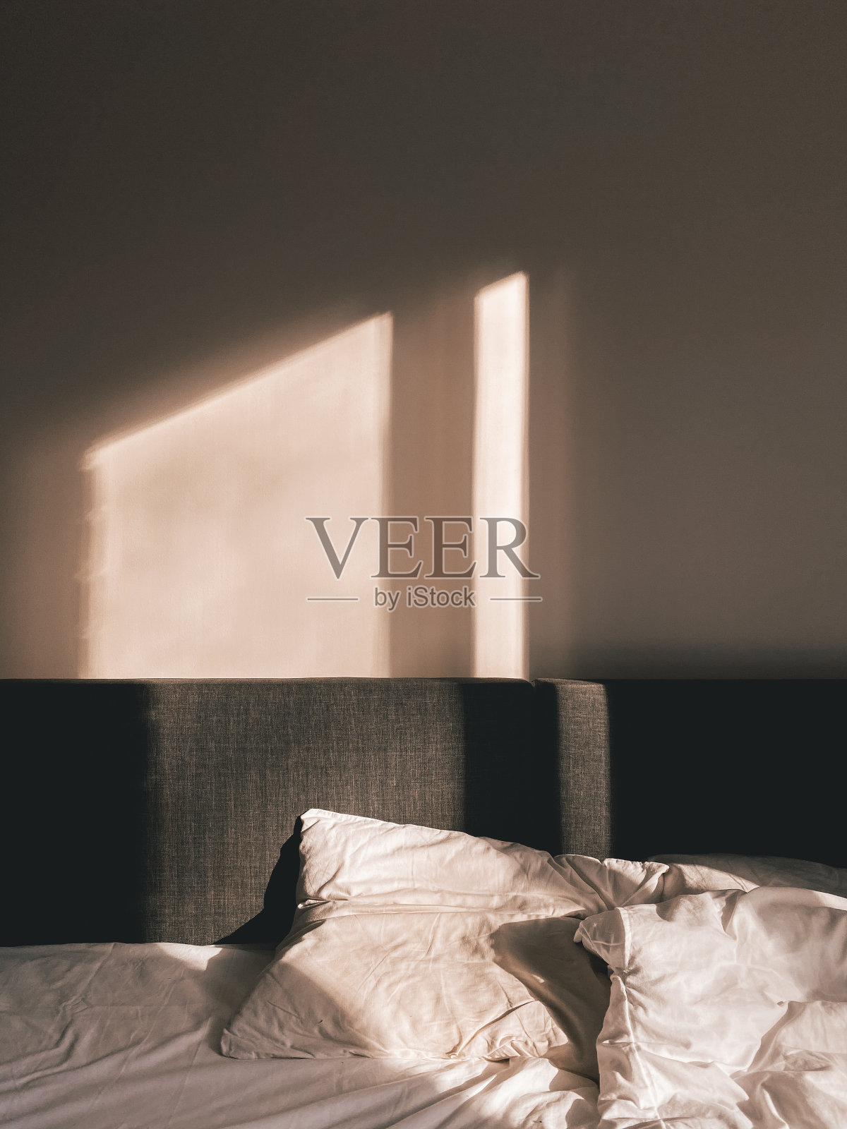 卧室里有一张灰色的床和白色的枕头,秋天的阳光从窗户照进来照片摄影图片