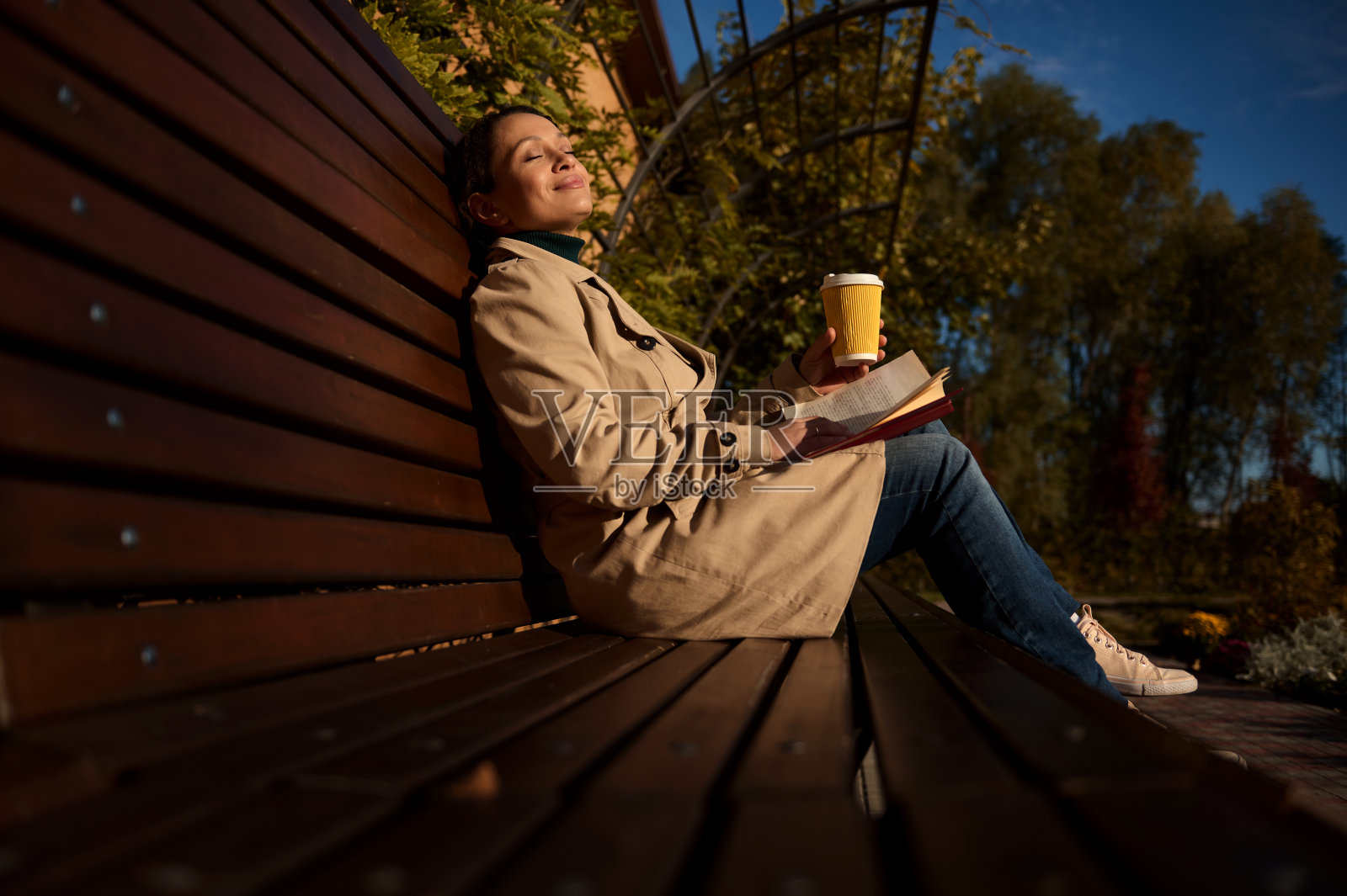 公园里,一位美女闭着眼睛坐在木凳上,端着纸杯热饮和一本书,享受着秋日的阳光,远离城市的喧嚣,远离电子产品照片摄影图片