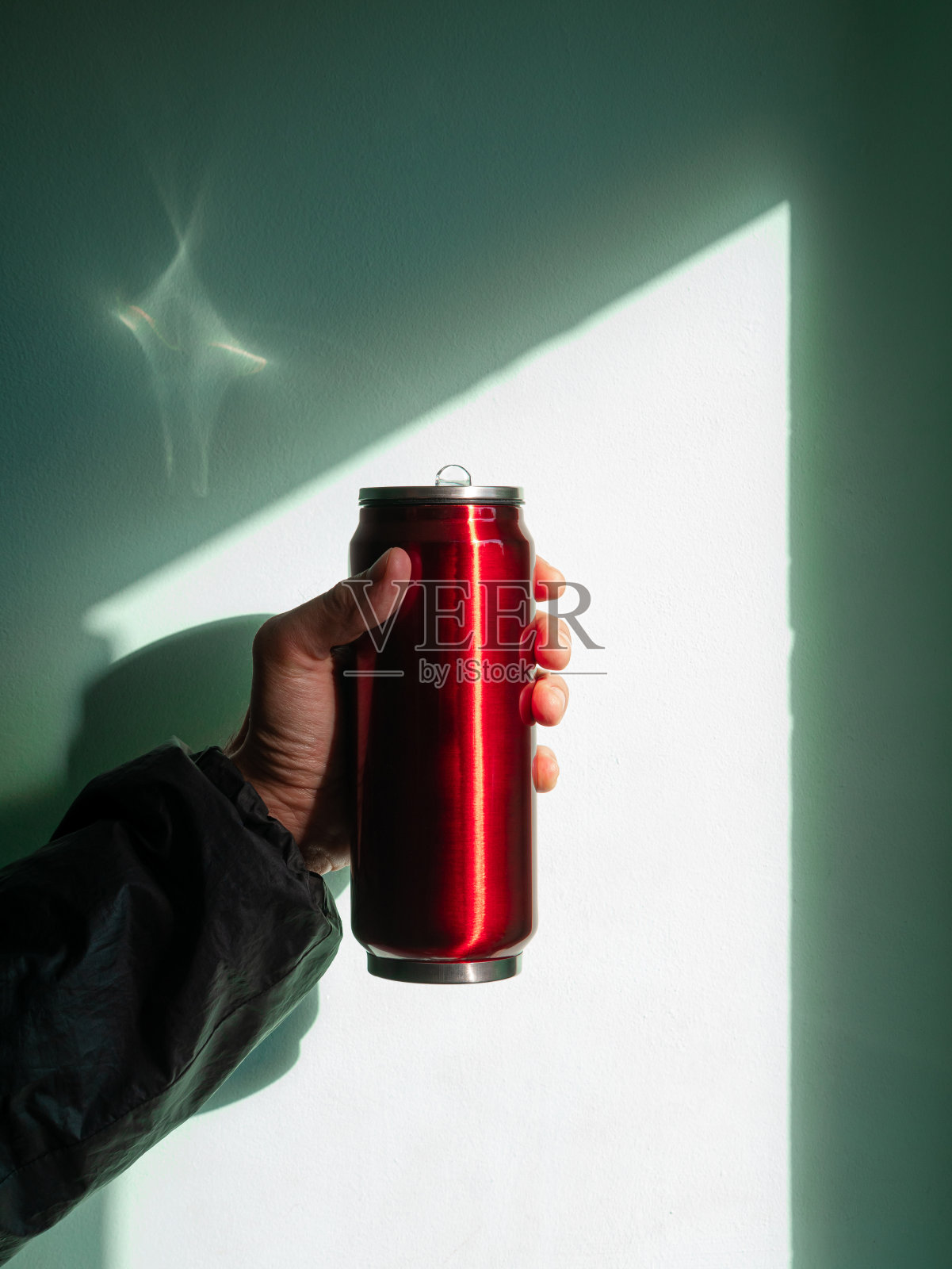 红色的热水瓶在男性手中靠在墙上,阴影刺眼。在寒冷的秋冬天气喝热茶和咖啡照片摄影图片