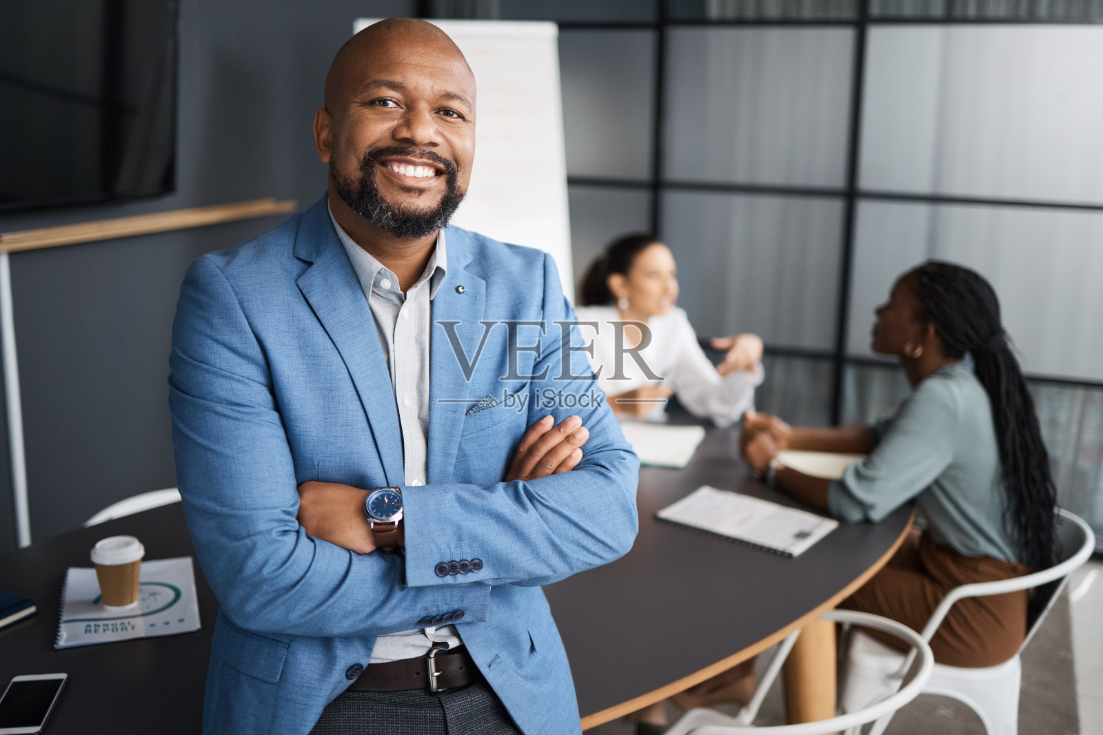 一位成熟的商人双臂交叉站在会议室里,背景是他的同事照片摄影图片