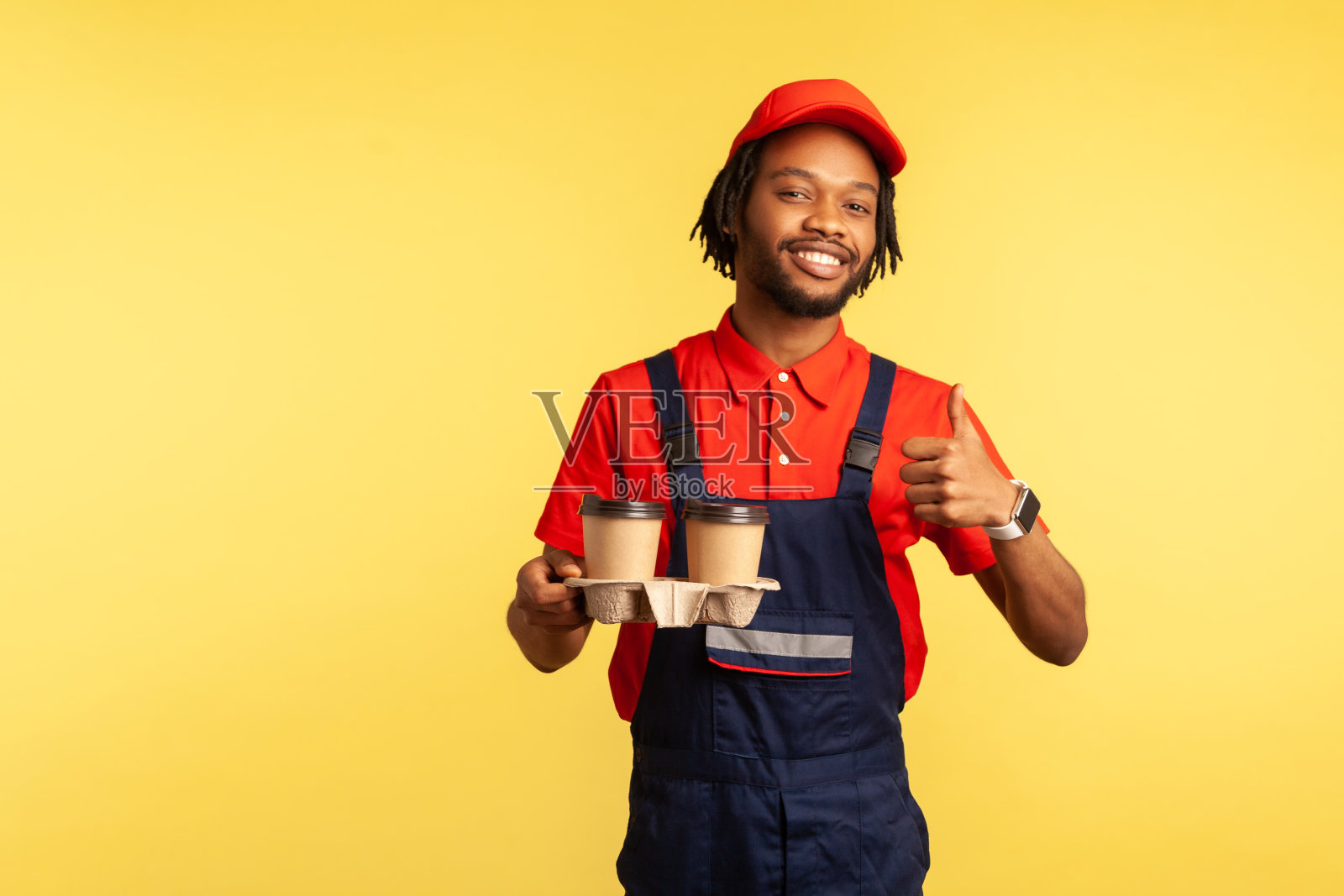 快递员拿着咖啡,用一次性杯子提供饮料,竖起大拇指,诸如此类的手势。照片摄影图片