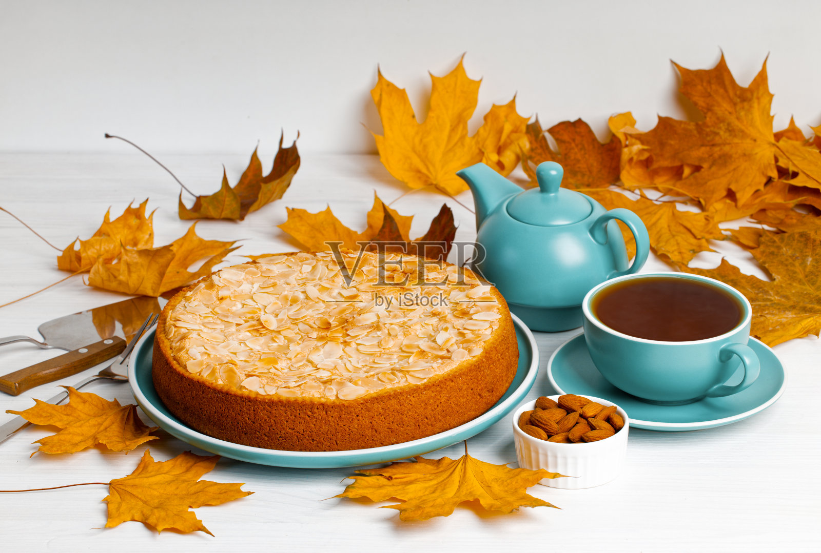 白色木桌上摆着装饰着杏仁花瓣、茶和秋叶的自制浆果派。浅的焦点。照片摄影图片