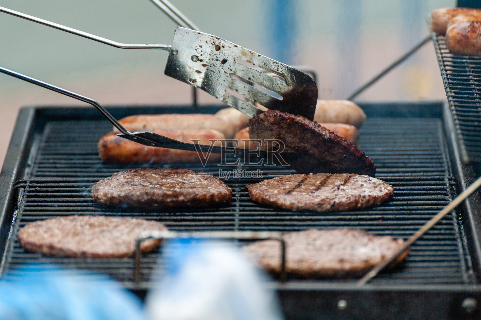 在大型户外烧烤上烤着汉堡和香肠。面包袋在前景中失去了焦点。照片摄影图片