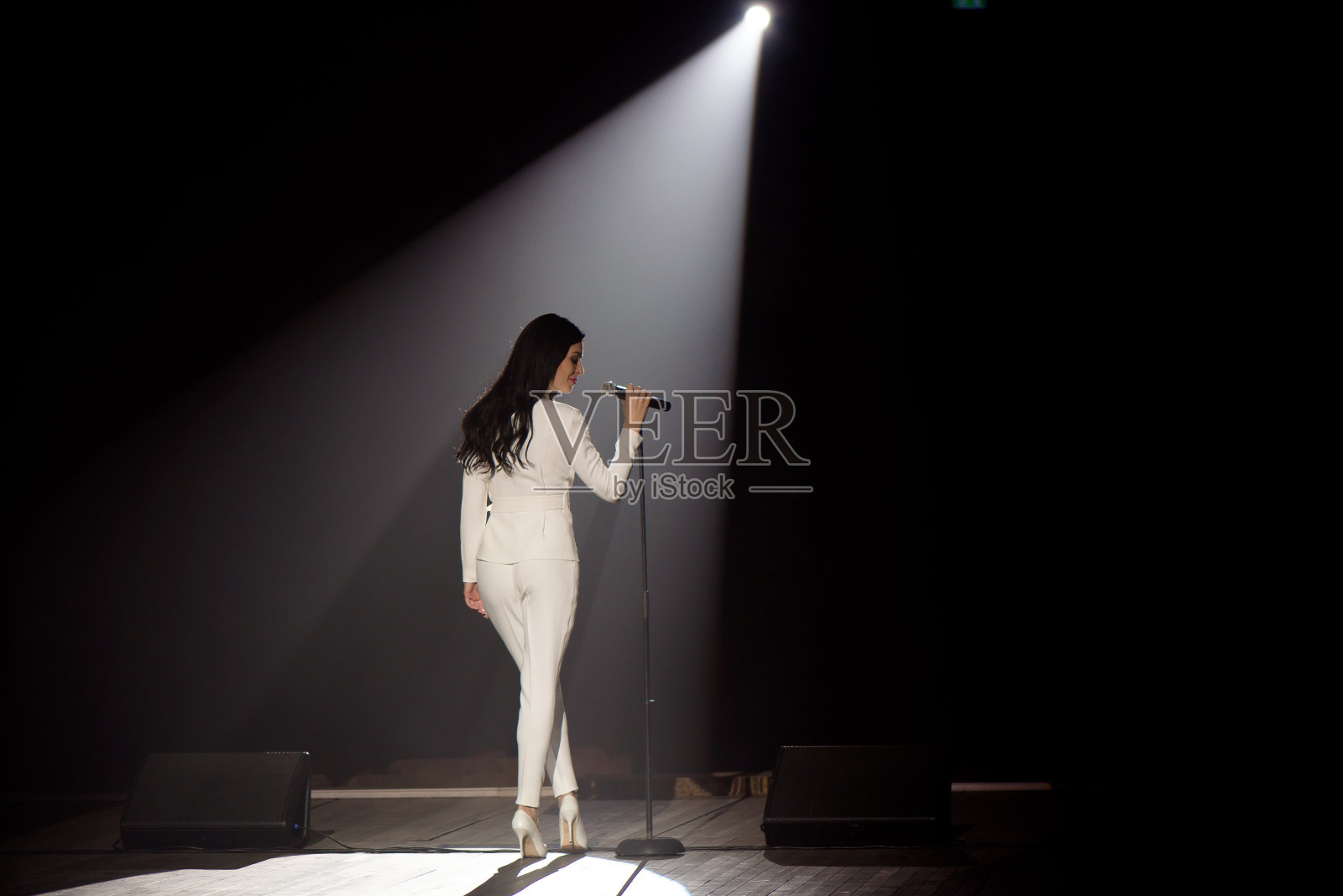 歌手在舞台上的一束白光中。照片摄影图片