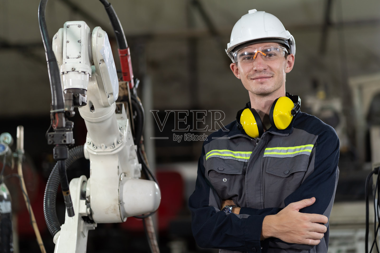 男工程师工人的肖像站在工厂的自动机械臂机器附近。男性技术工人在智能工厂使用自动机械手工作照片摄影图片