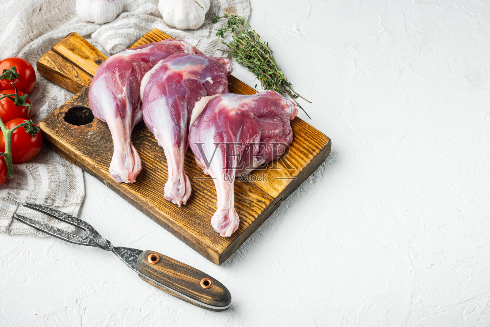 Free Range Farm Duck Legs, with herbs and配料,木制砧板上,白色石头背景上,有文字和文字空间照片摄影图片