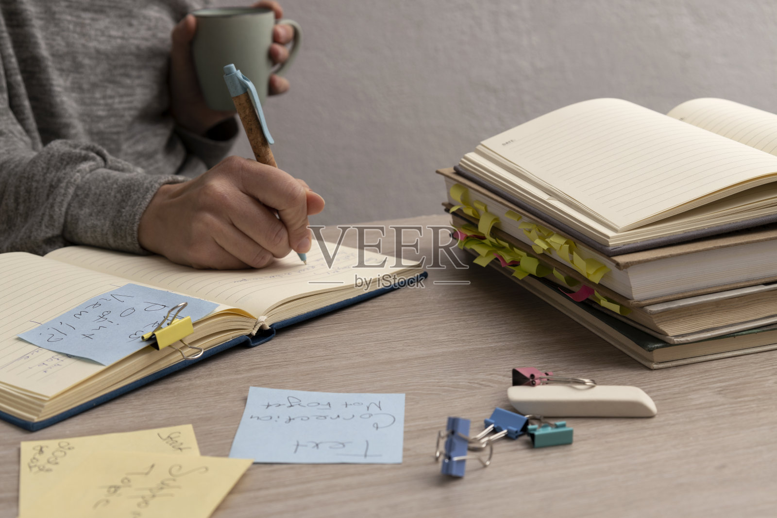 为商业广告写文字的女人。工作场所和一堆书、纸、文具,女人拿着杯子和笔,写下想法照片摄影图片