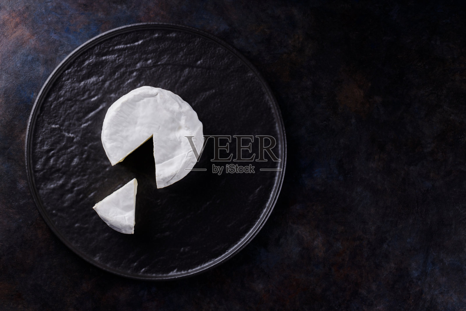 黑色背景下的卡门培尔乳酪。黑色盘子上有白色霉菌的软奶酪。极简主义。本空间照片摄影图片