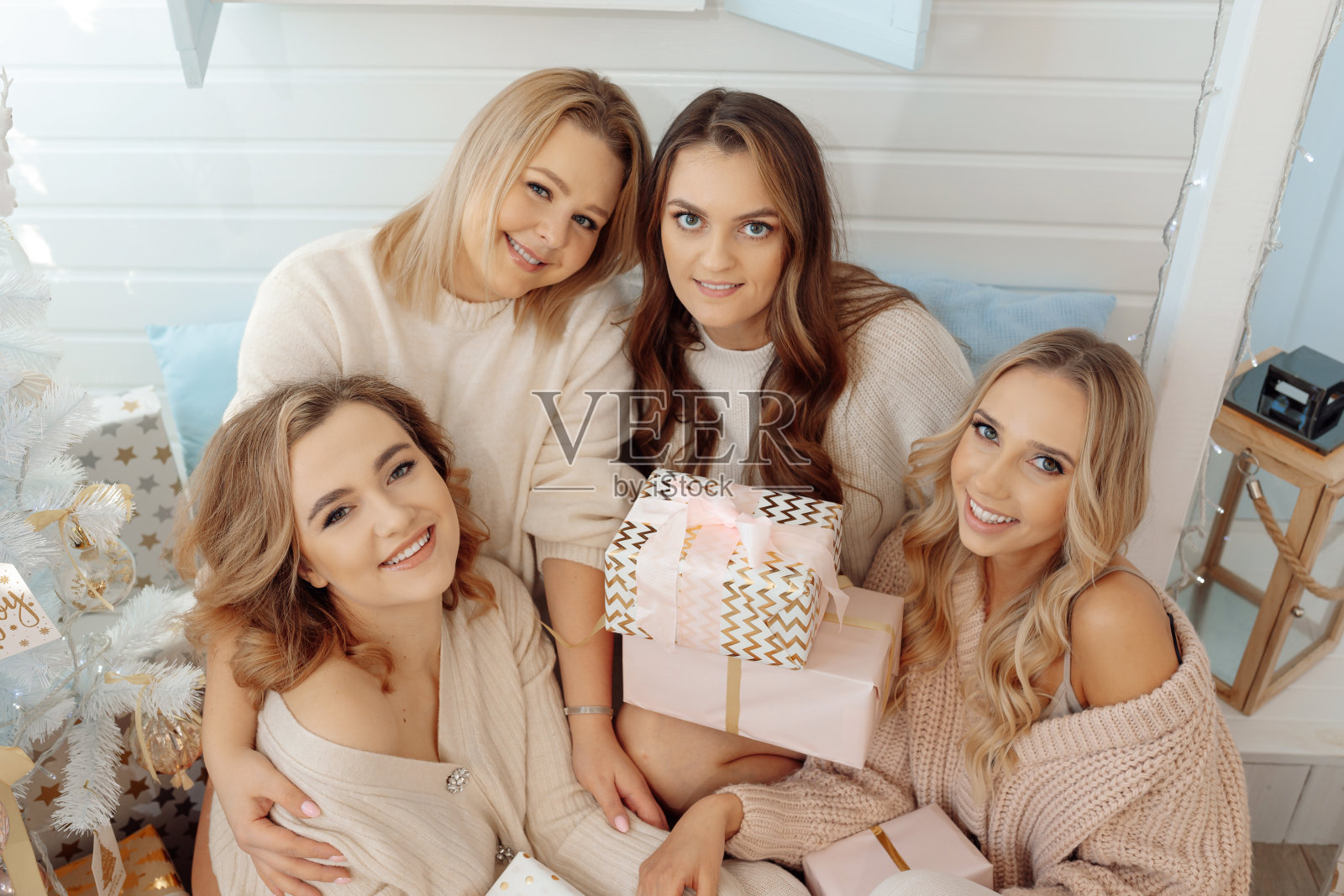 4名年轻女子在圣诞树旁聚会。在新年的装饰中,幸福,微笑,节日礼物。照片摄影图片