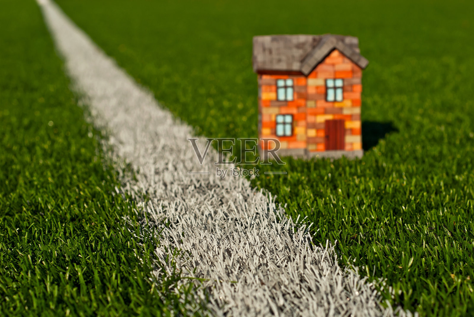 草地上的砖玩具房子。绿色草地上的橘黄色房子。自己的住房和建筑的概念。草地上的白色条纹模仿道路。照片摄影图片