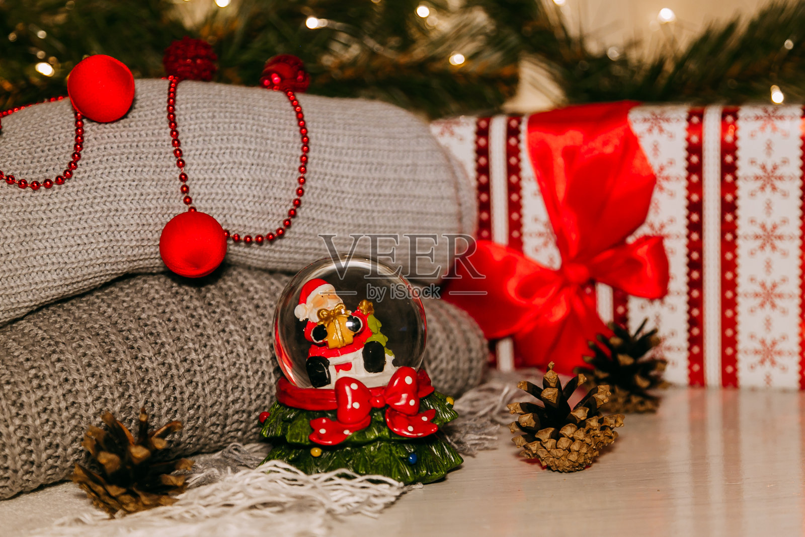 红色的圣诞树玩具和云杉树枝在雪地上,背景上织着灰色的毛衣和花环照片摄影图片