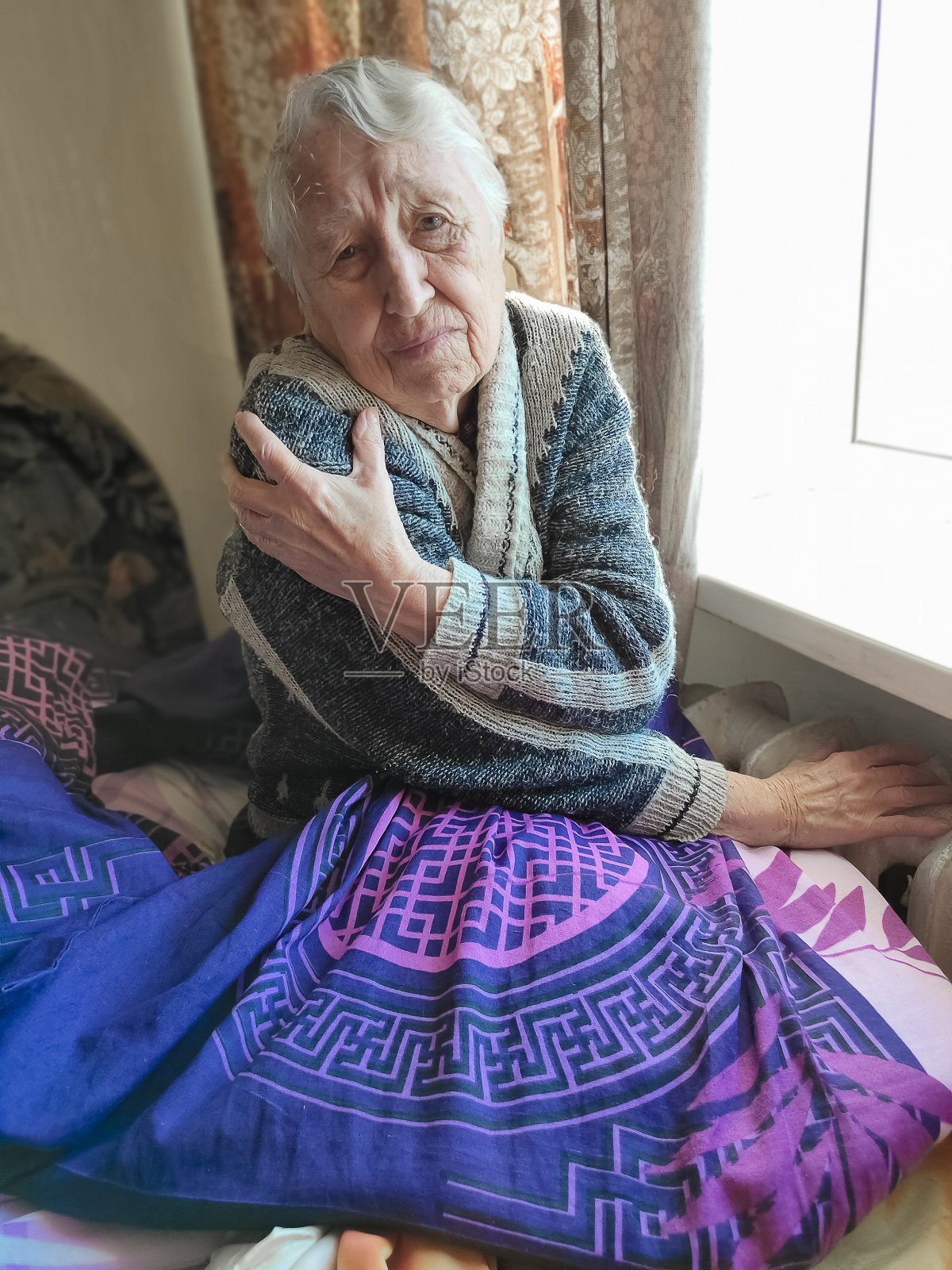 在暖气片前拿着煤气费的老妇人。支付冬季取暖费用。照片摄影图片