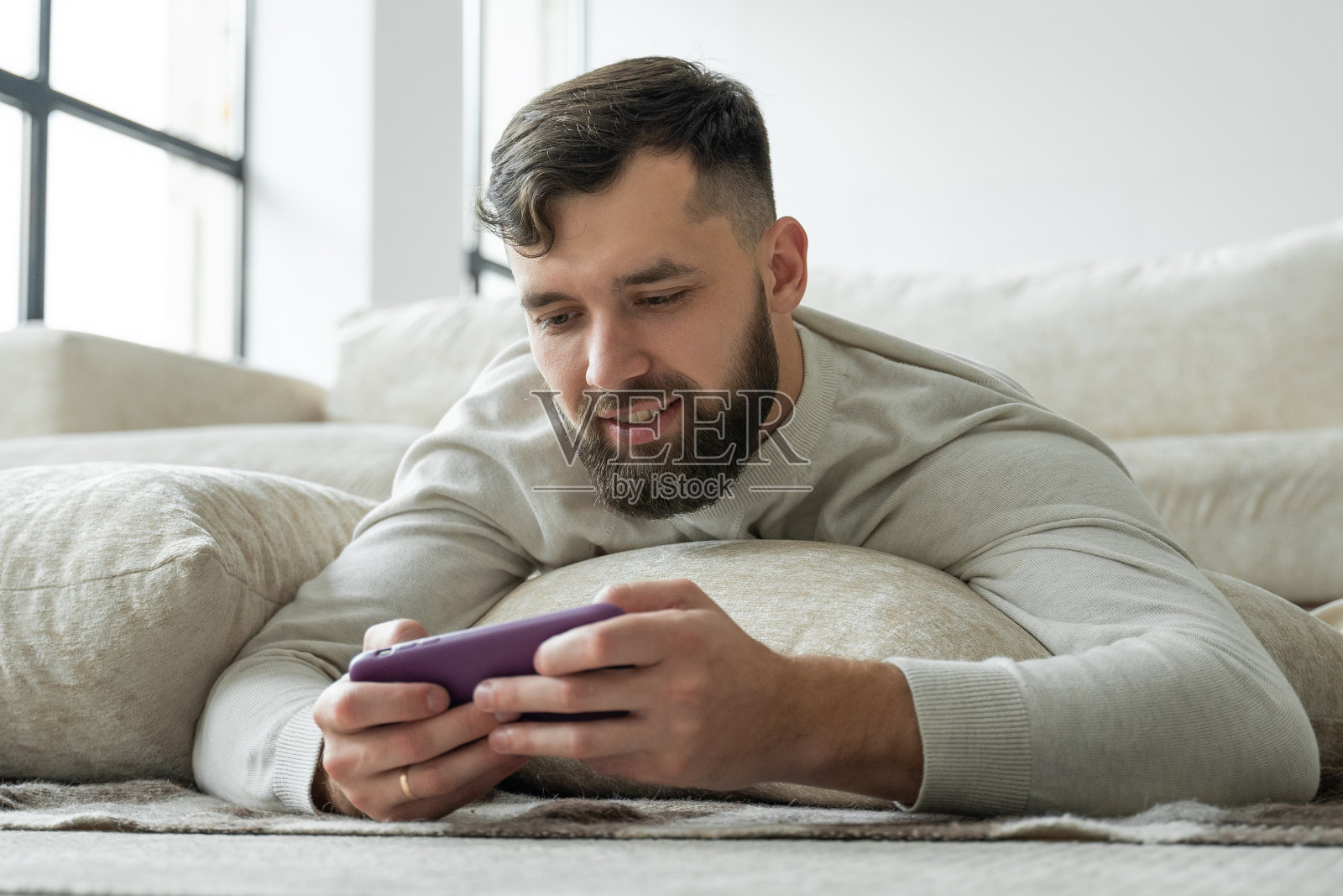 一幅激动的留着胡子的年轻男子的画像,他躺在地板上,用手机玩游戏照片摄影图片