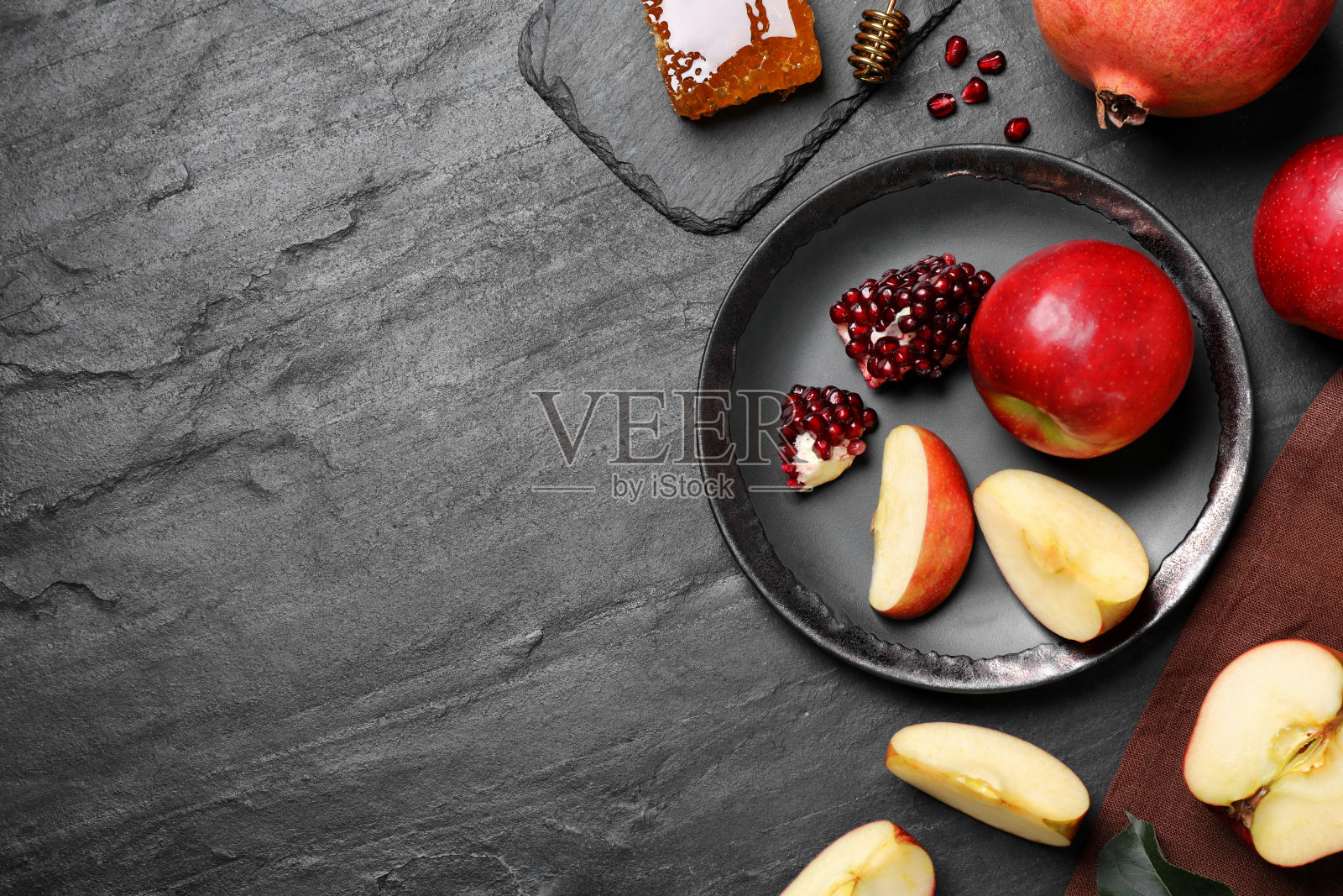 蜂蜜、苹果和石榴放在黑色的桌子上,平放有文字空间。犹太新年假期照片摄影图片