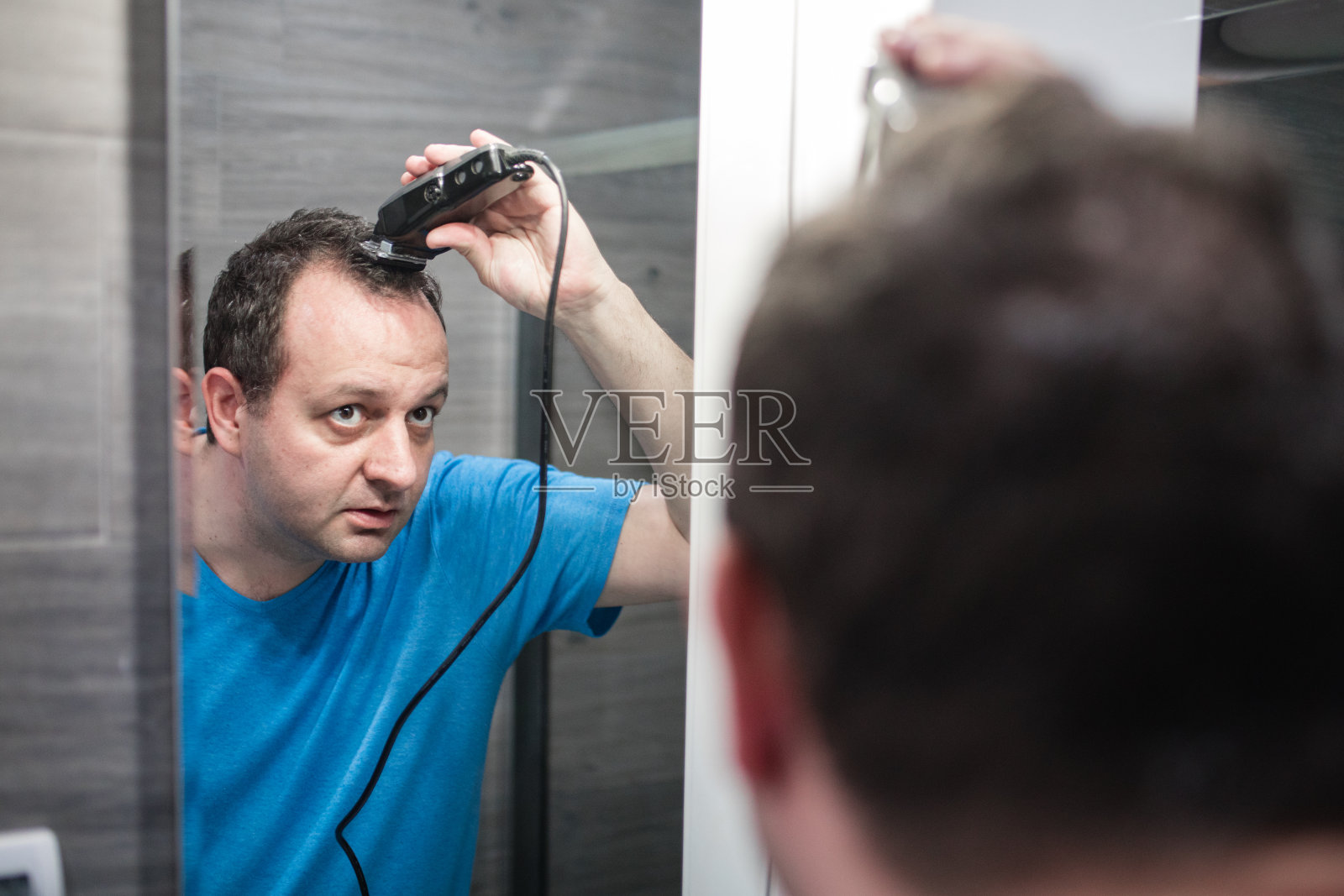 一名穿着t恤的男子在浴室的镜子前用理发器给自己理发,这是一种隔离的新冠病毒大流行covid - 19的概念照片摄影图片