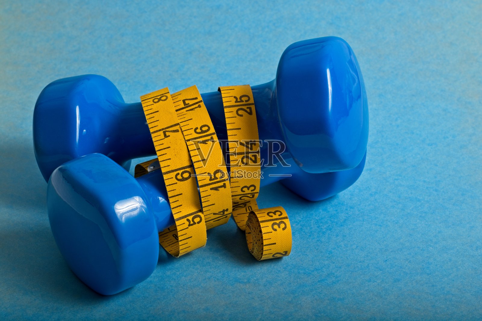 蓝色表面上交叉着的哑铃被黄色的卷尺包裹着照片摄影图片